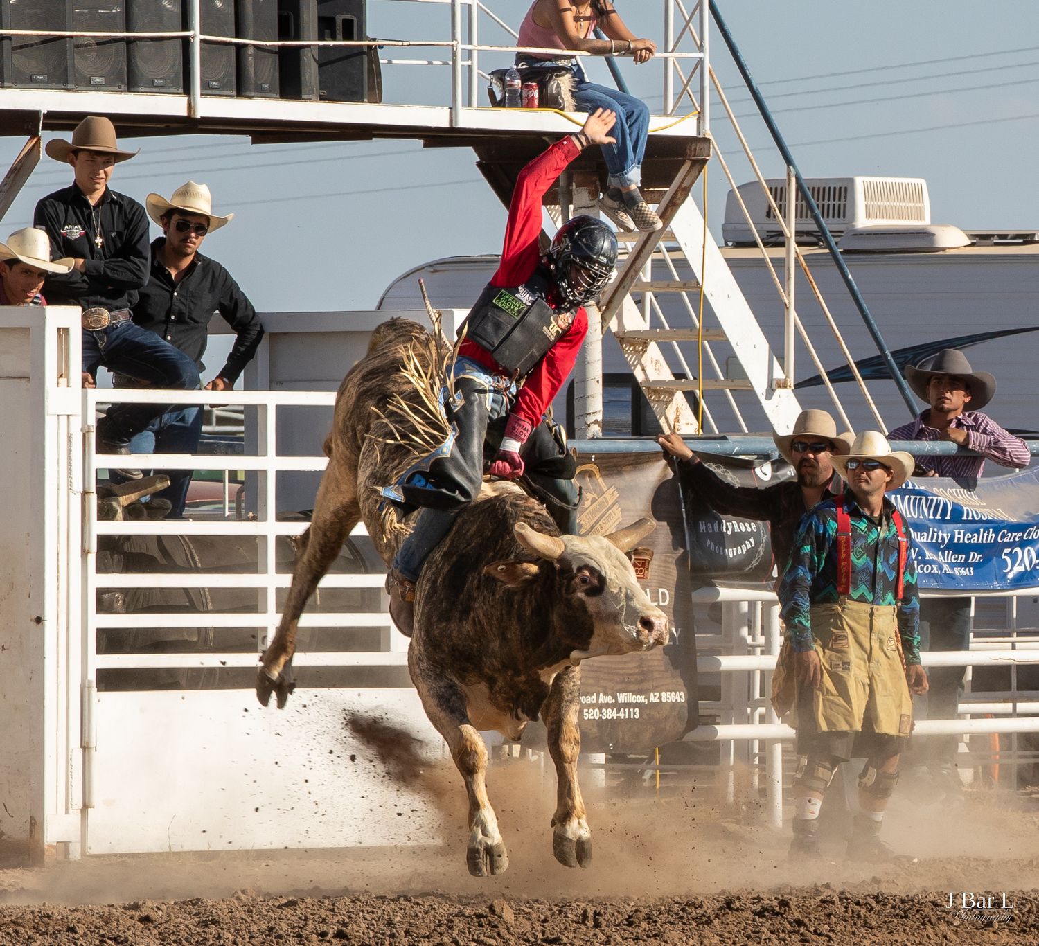 Bull rider in red gear holding on during a powerful bull ride at a rodeo event.