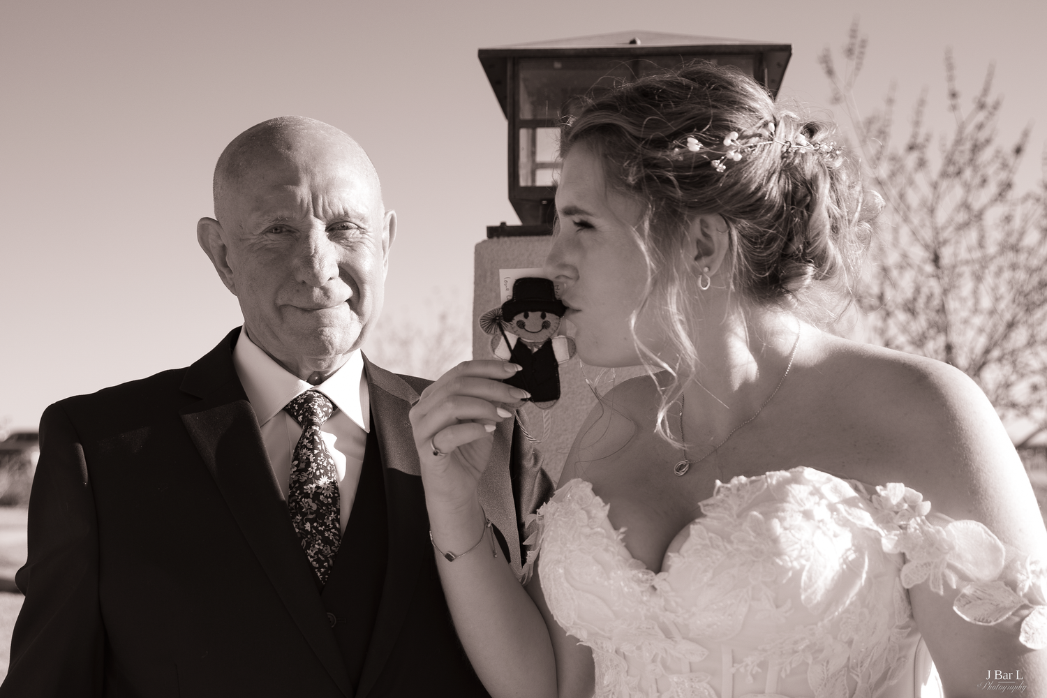 Bride and elderly gentleman share a tender moment examining a small photo in sepia-toned portrait.