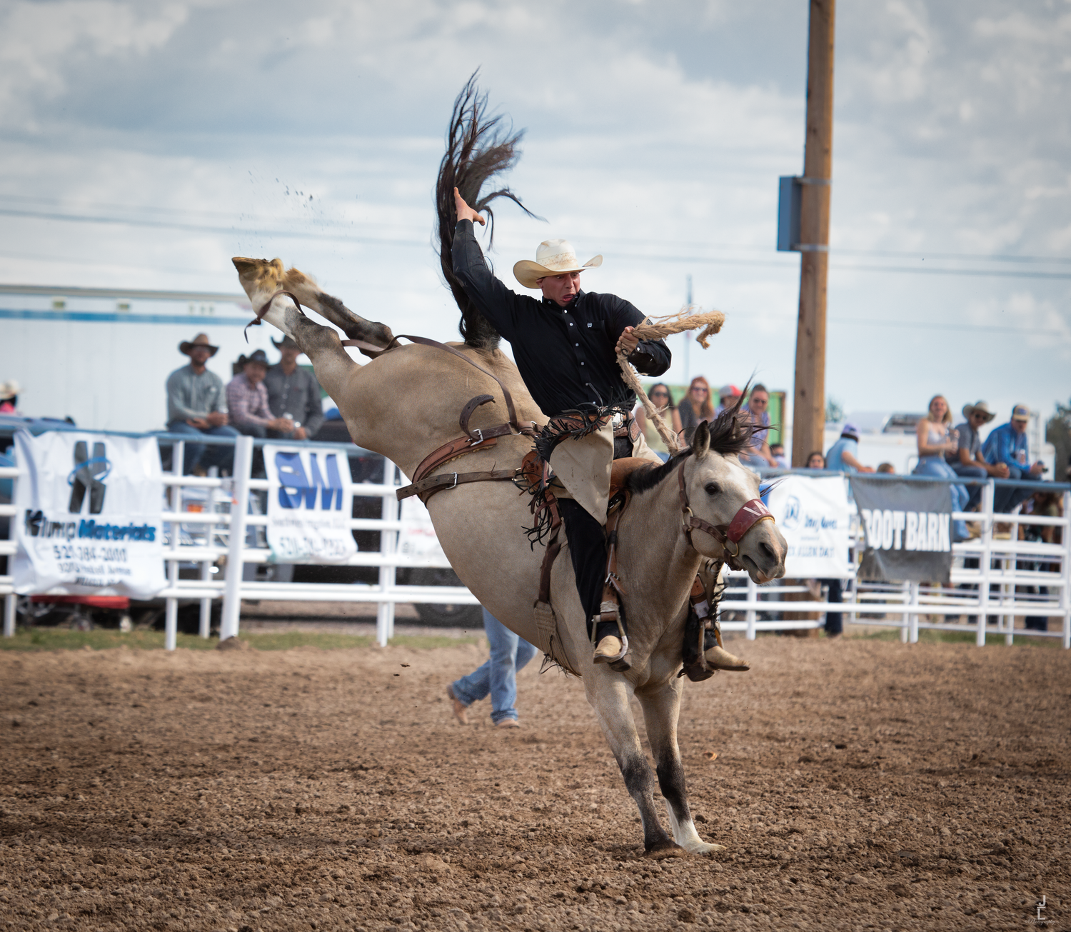 Cowboy rides a bucking bronco high in the air during a competitive rodeo event under cloudy skies.