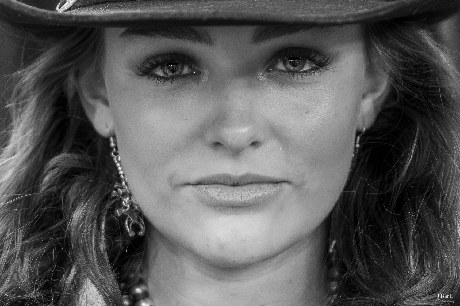 Close-up black and white portrait of a woman wearing a cowboy hat and dangling earrings.