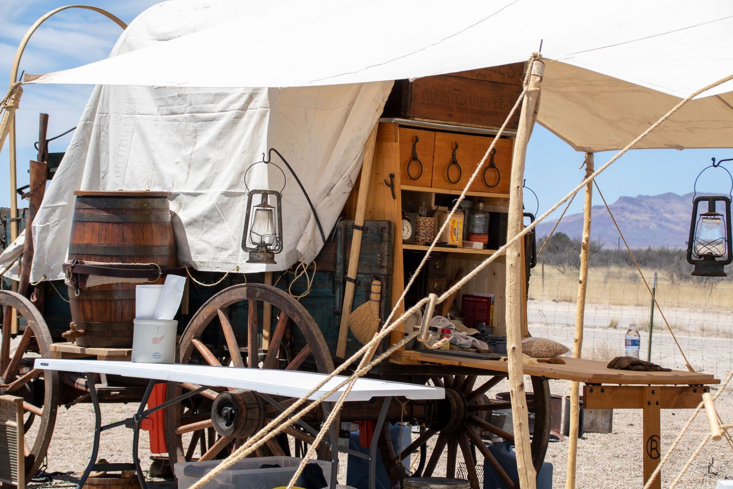 A vintage covered wagon with wooden barrel, lantern, and western tools at an outdoor display.