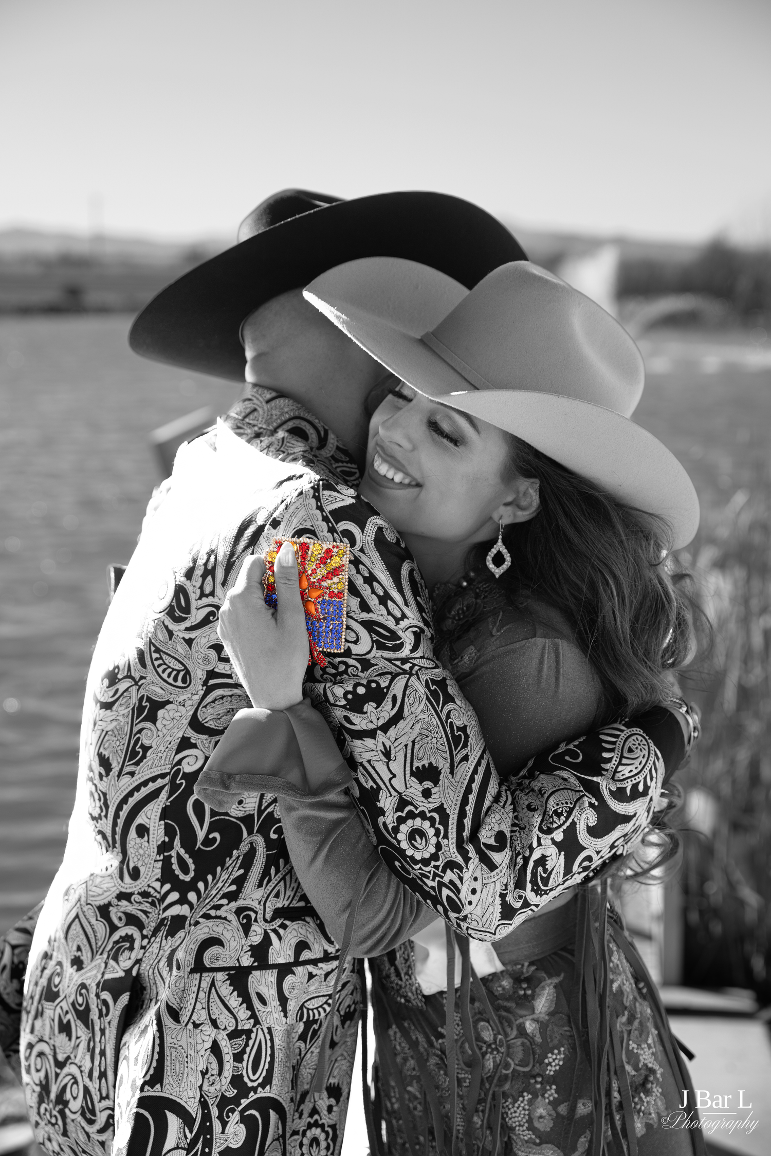 Black and white photo of two women in cowboy hats sharing a warm embrace outdoors.