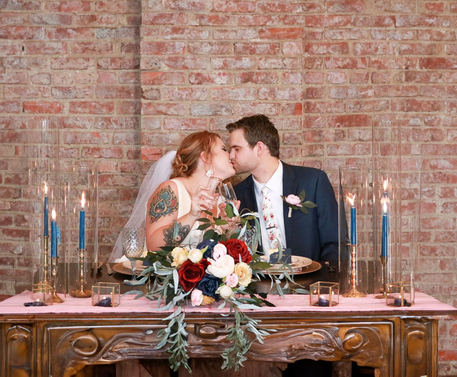 Bride and groom sitting at dinner table kissing and clinking Champaigne glass.