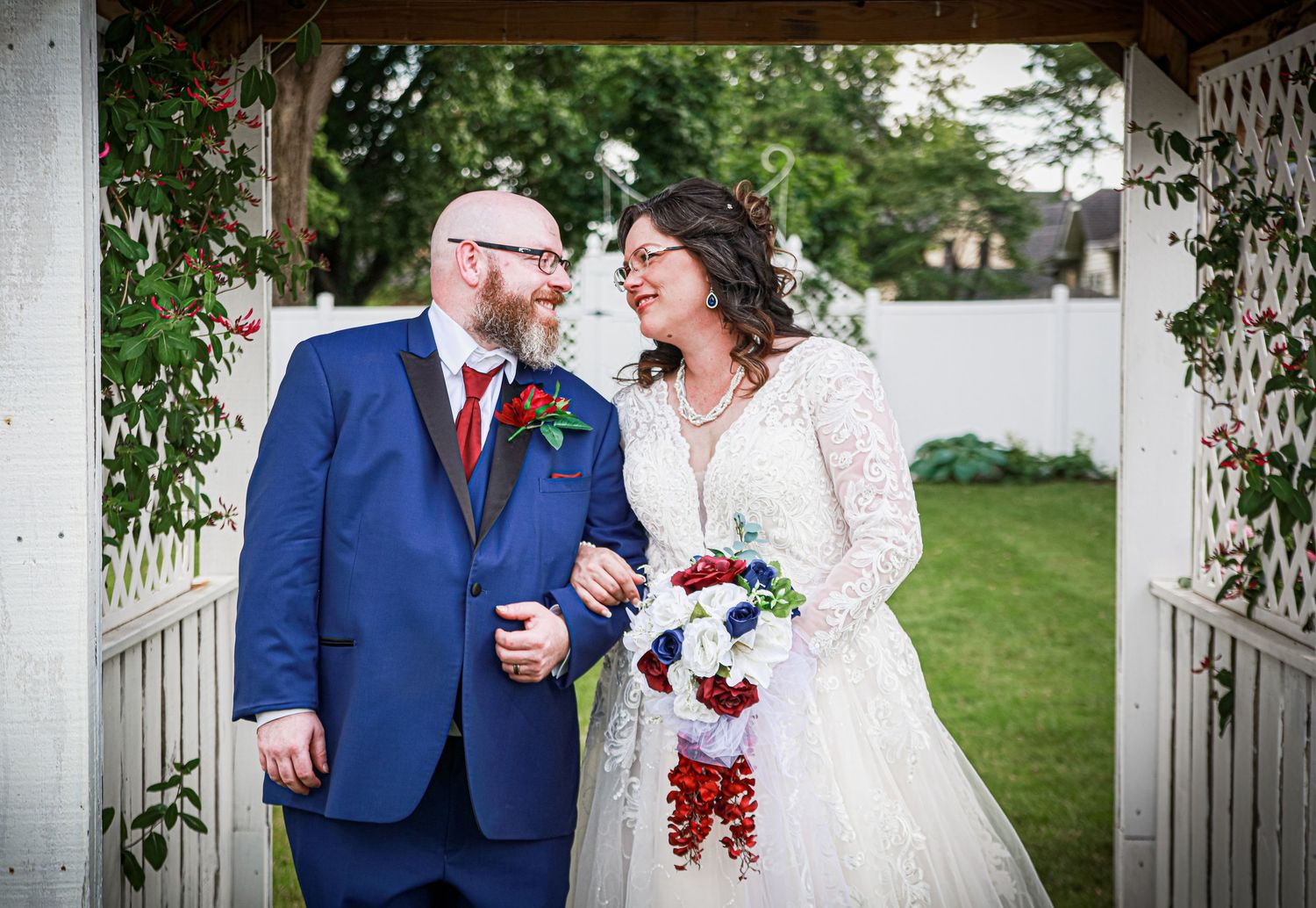 Groom and bride standing under arch, gazing at each other in love.