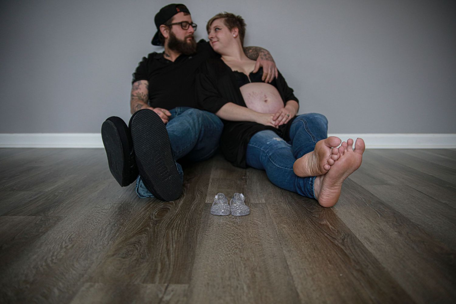 Man and pregnant woman sitting on floor with baby shoes.