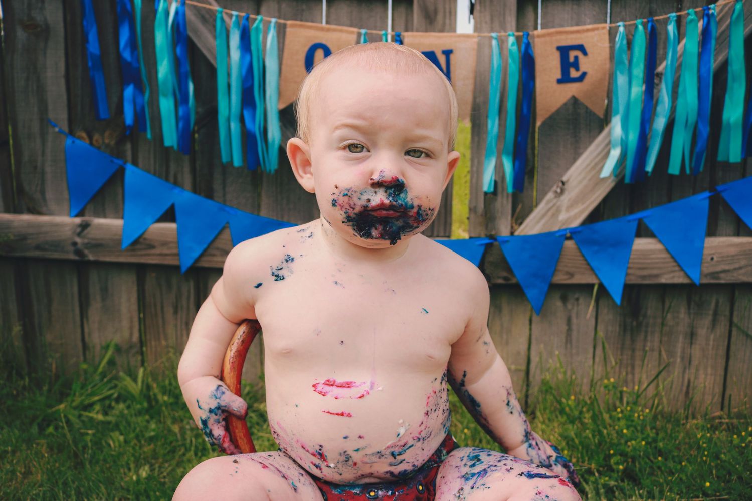 One year old birthday boy sitting outside with cake on his face.