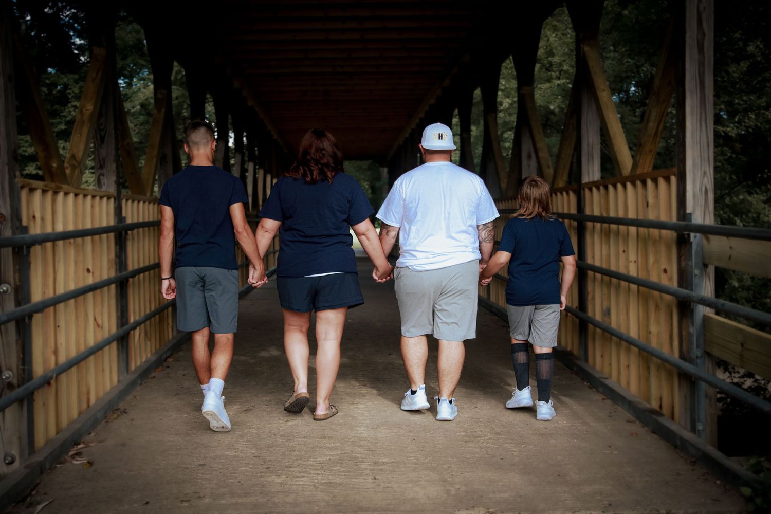 Family of four holding hands and walking away on bridge.