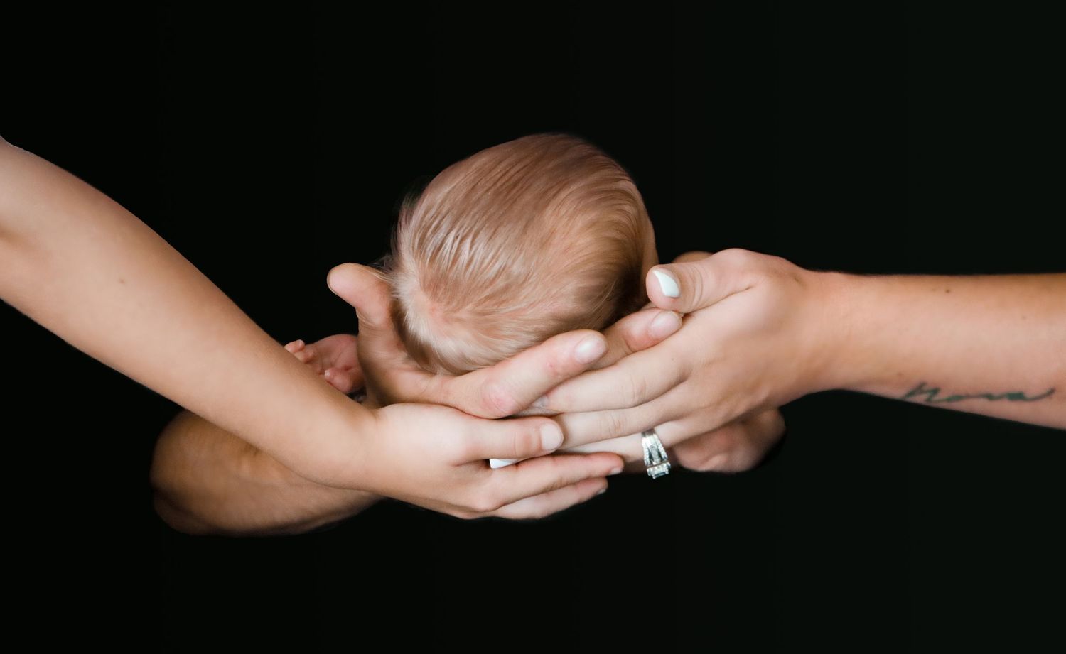 Infant being gently held by mom, dad, and sibling at an in-home newborn session in Indianapolis, IN.