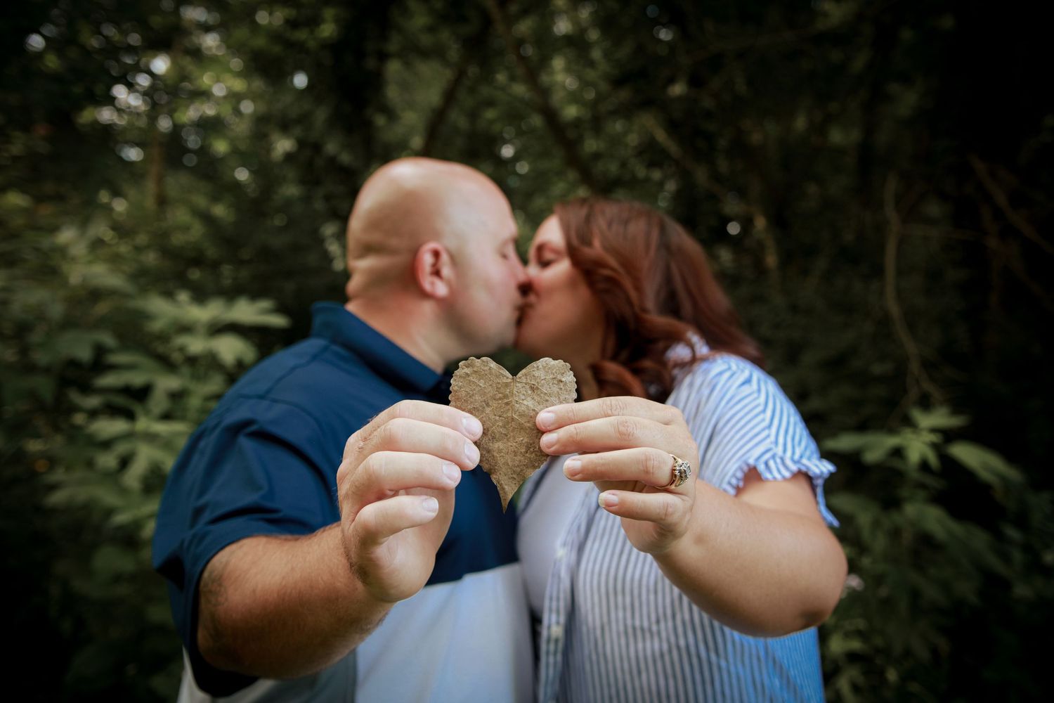 Husband and wife holding heart leaf and kissing at the park during autumn.