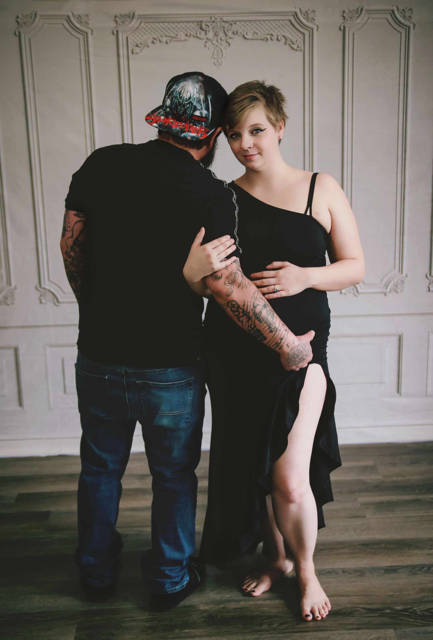 Woman in black dress holding onto man who is grasping her pregnant belly.