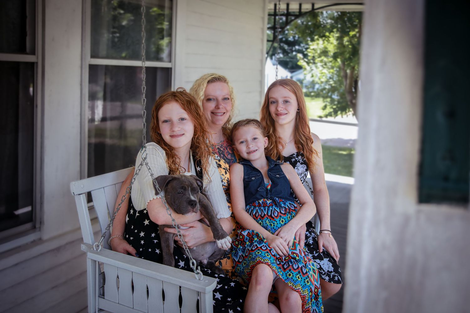 Mom and daughters sitting on porch swing with new puppy in Connersville, IN.