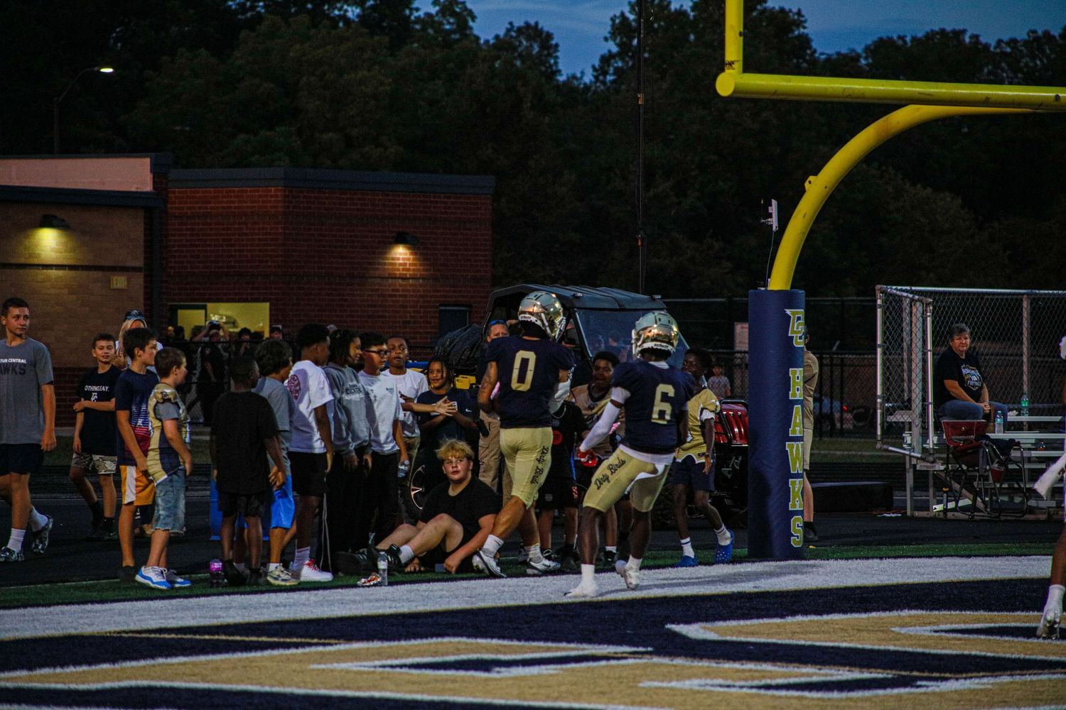 Football players in navy uniforms near the end zone goalpost during an evening high school football game.
