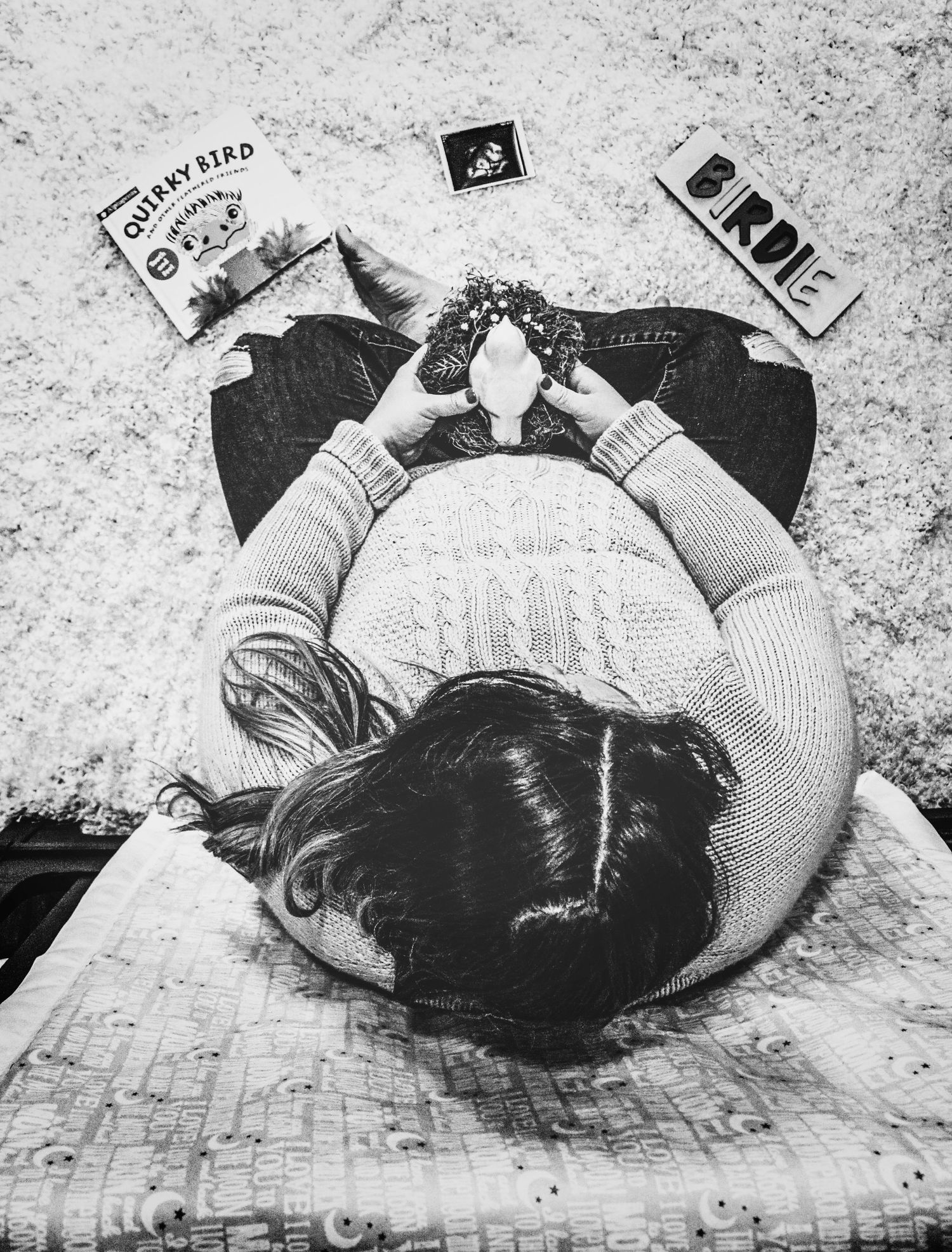 Black and white aerial maternity photo of pregnant woman lying down surrounded by baby name signs.