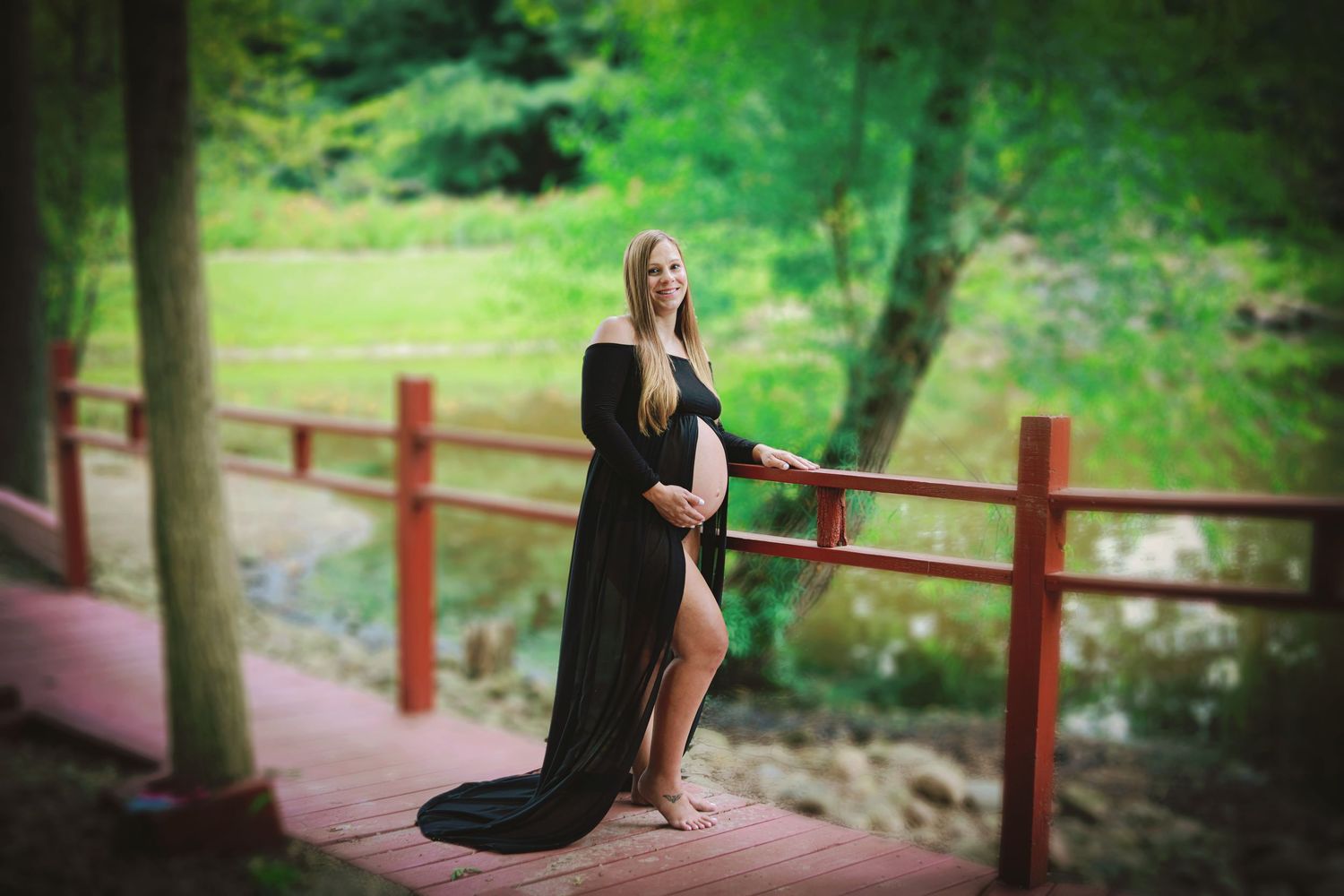 Pregnant woman wearing beautiful black dress on red bridge at Apple Works in Trafalgar, IN.