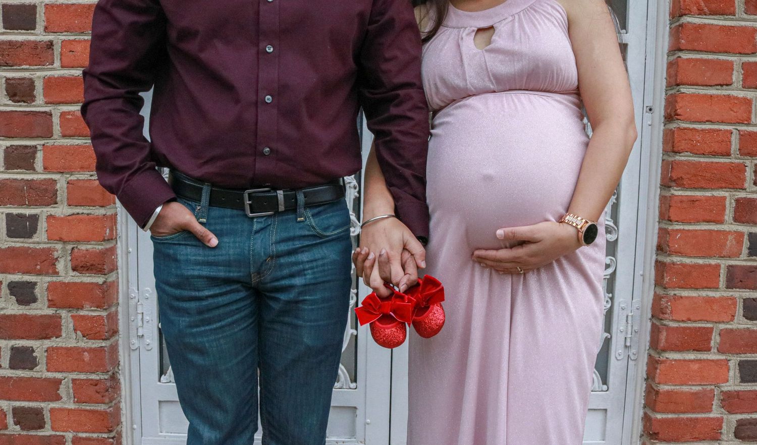 Man and woman holding hands with red baby shoes during pregnancy at Coxhall Gardens in Carmel, IN.