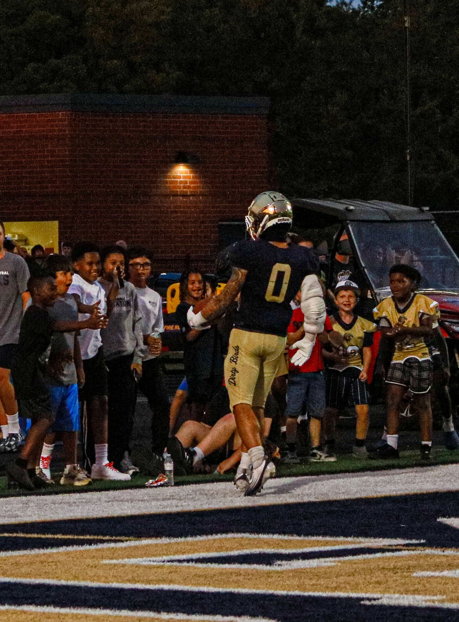 Football player wearing jersey number 0 celebrates near the end zone in front of cheering fans at a night game.