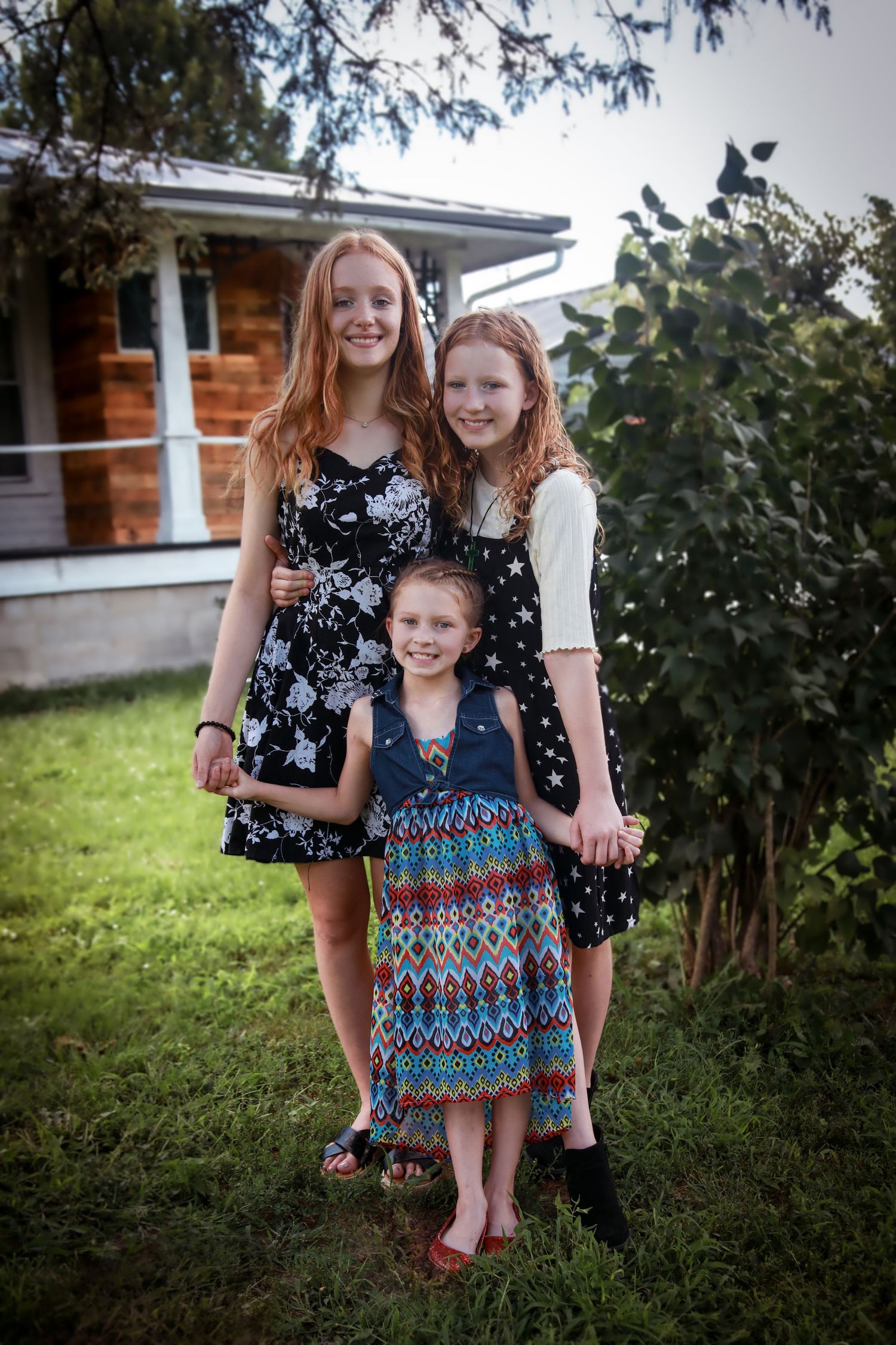 Three sisters standing together, holding hands in yard at a new home photoshoot in Connersville, IN.