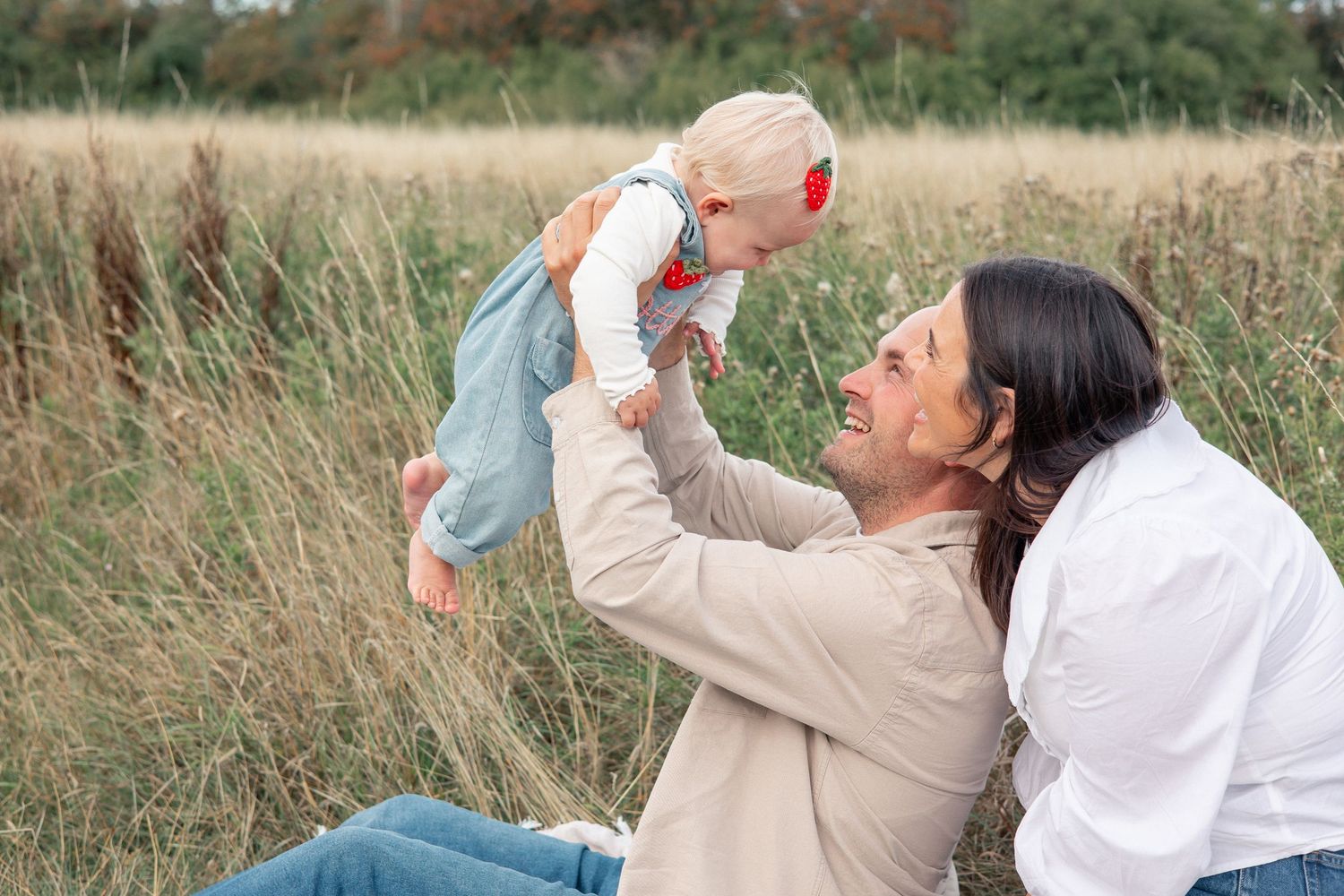 Couple enjoying a natural candid and playful moment together with their 1 year old in a sunny field in the Cotswolds, Stroud.