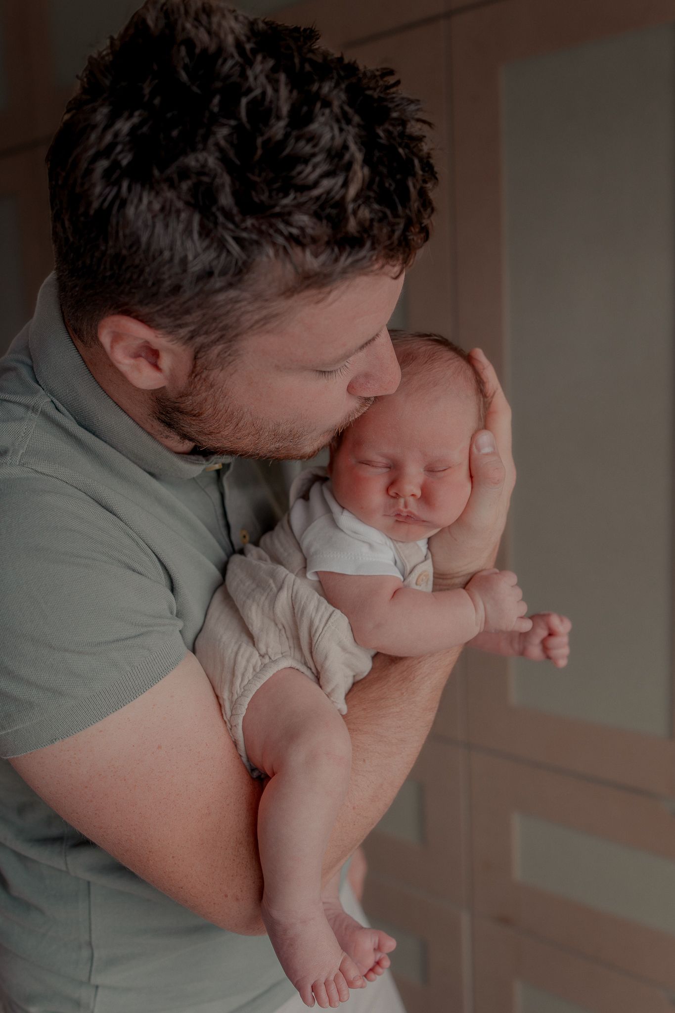 A father tenderly kisses his sleeping newborn baby while cradling the infant in his arms in Clifton, Bristol.
