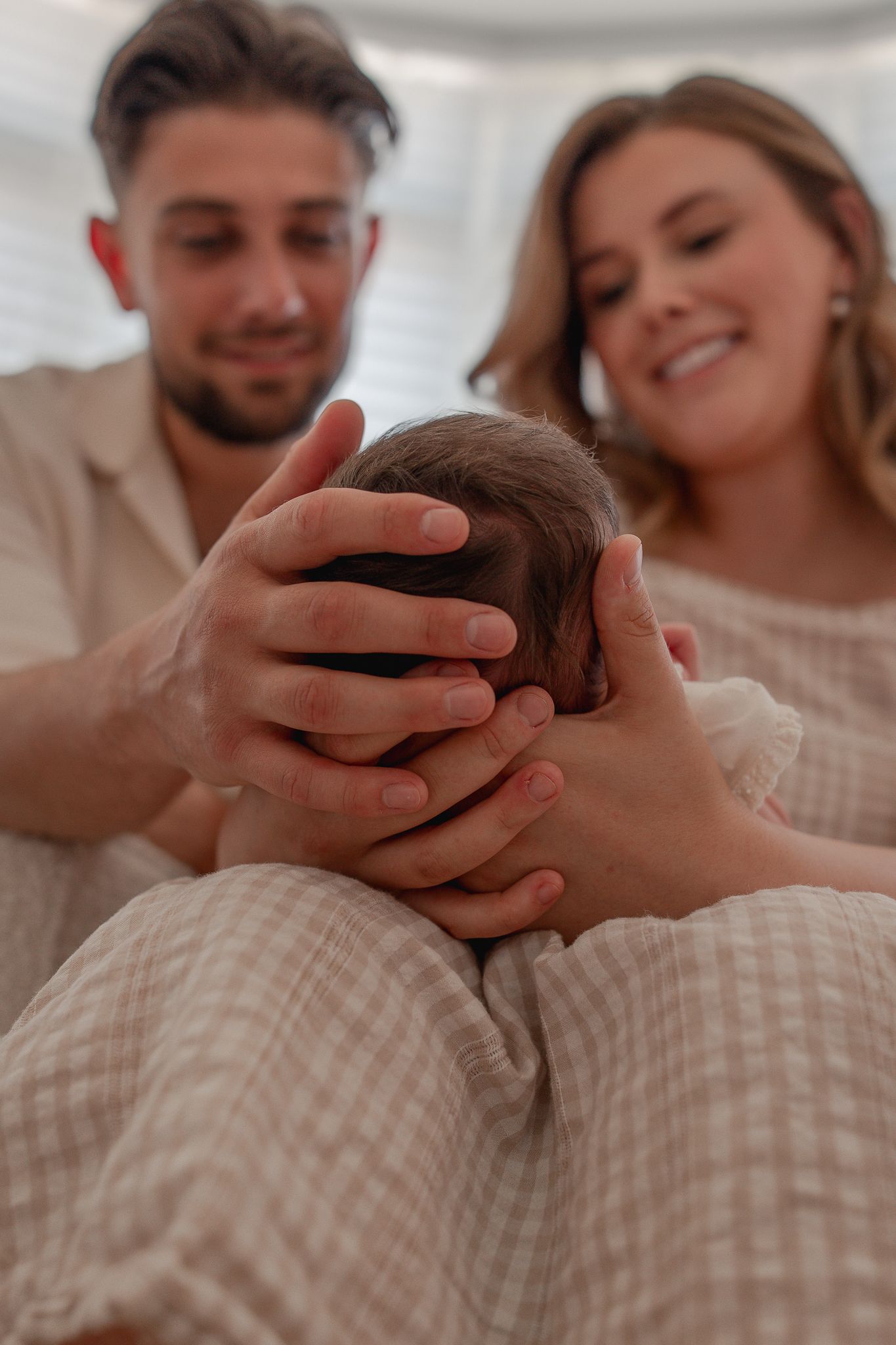 Happy parents gently cradling their newborn baby's head, sharing a tender family moment together for a Newborn Photoshoot in Widcombe.