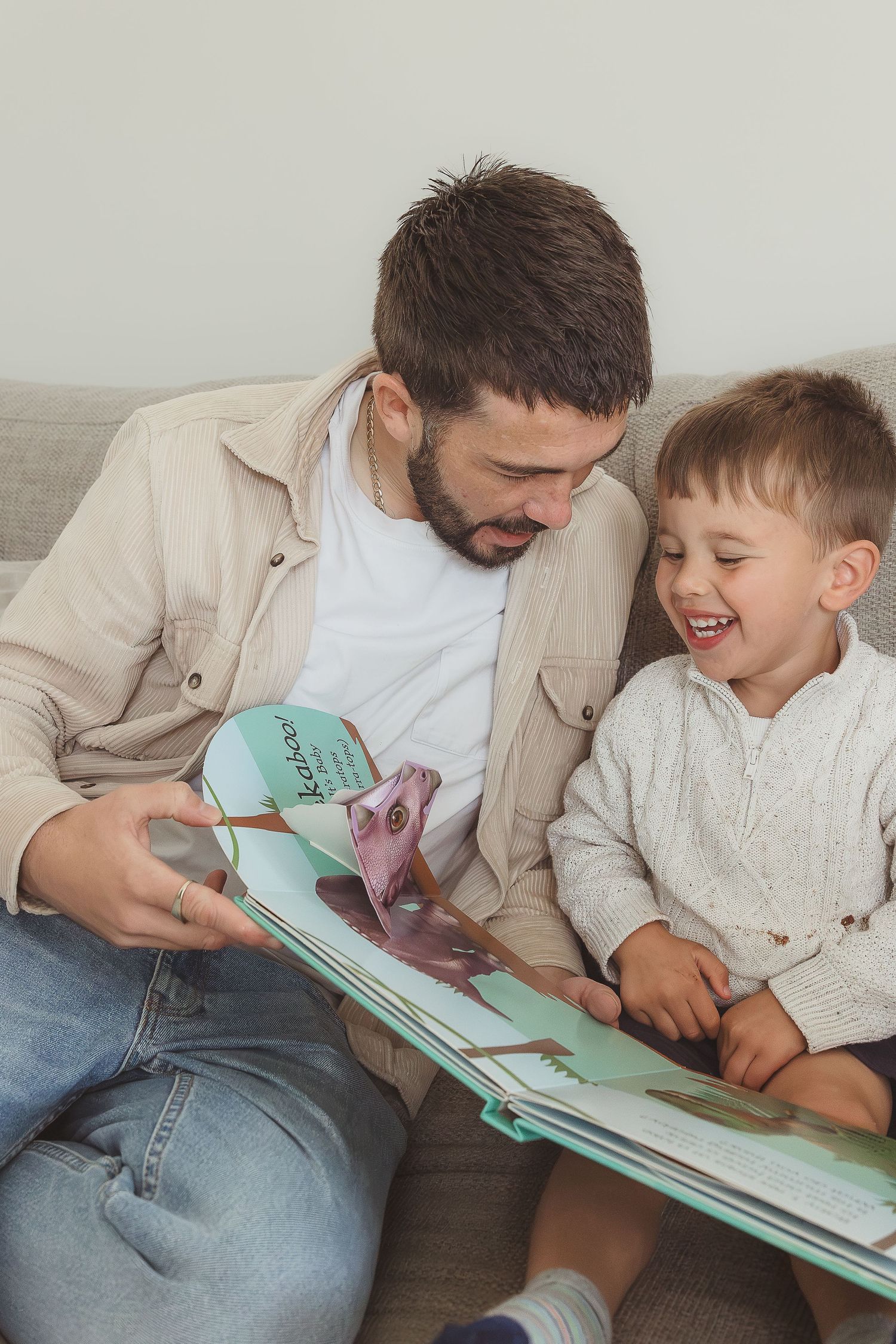 Family Photographer takes photo of dad and son reading a book at home in Bibury, Cotswolds.