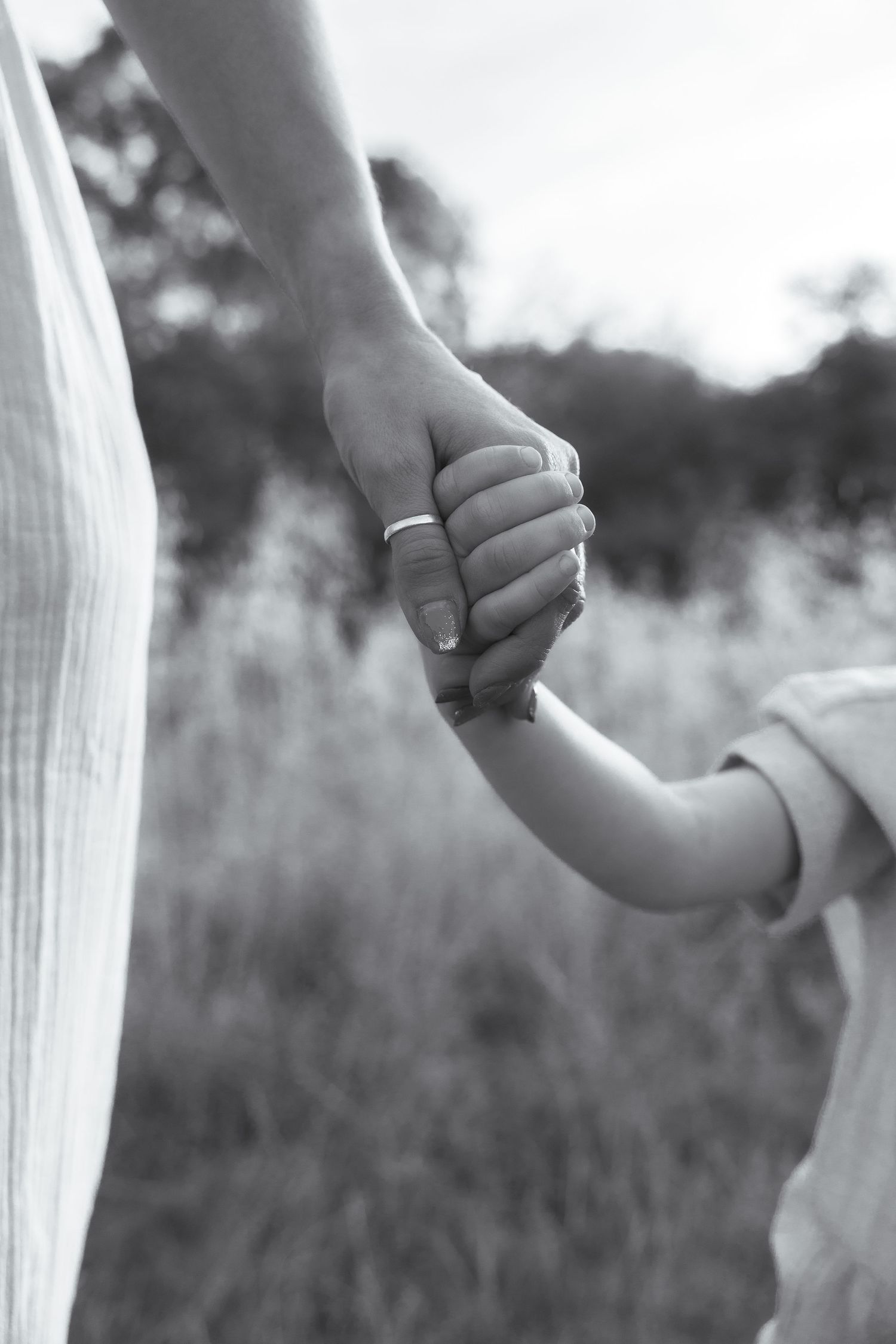 Black and white photo of a mother and child holding hands in a field, symbolising love and family bond in Snowhill, Cotswolds.