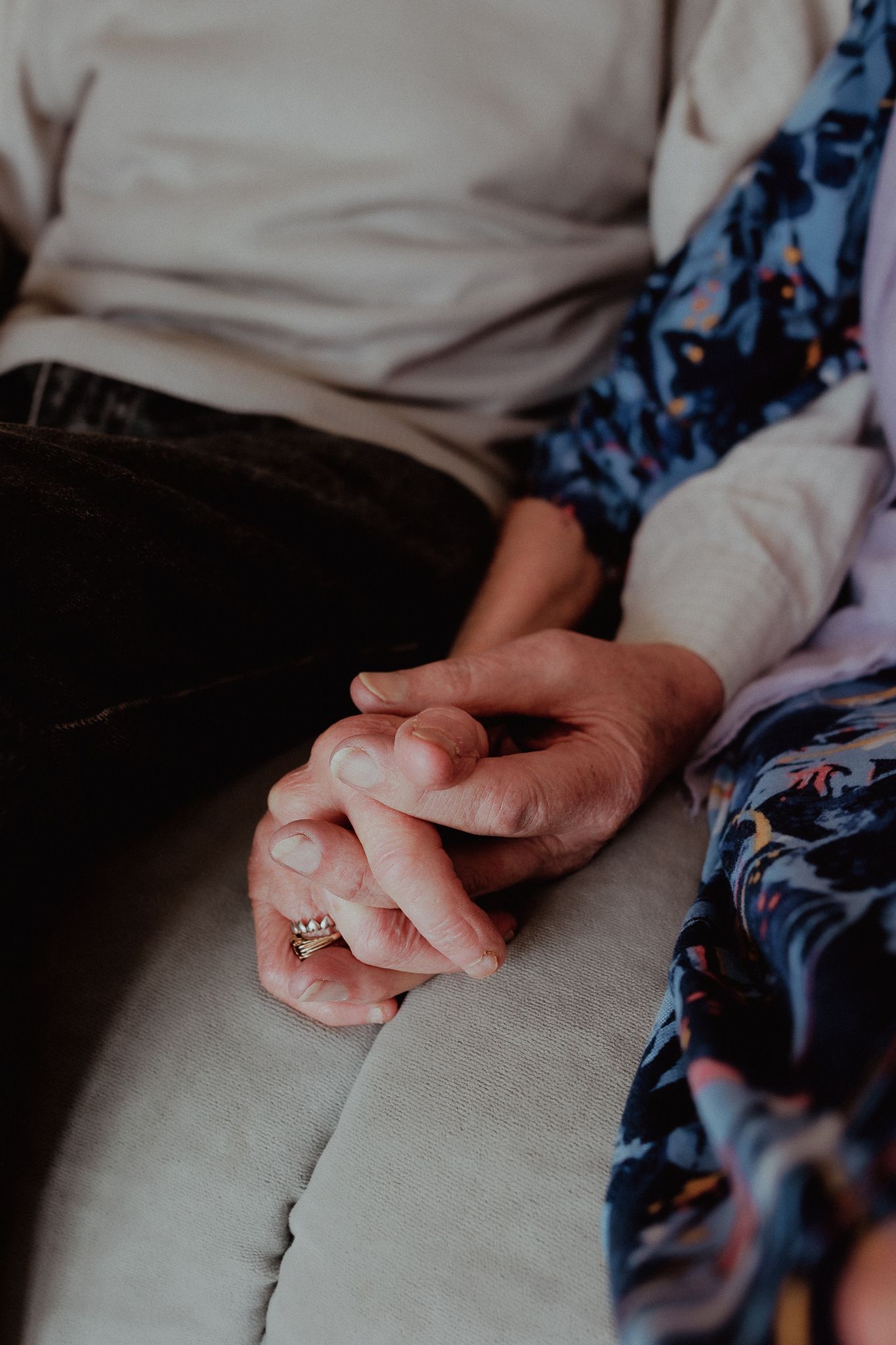 Close-up of elderly couple holding hands tenderly on a sofa in Barnsley, Cotswolds.