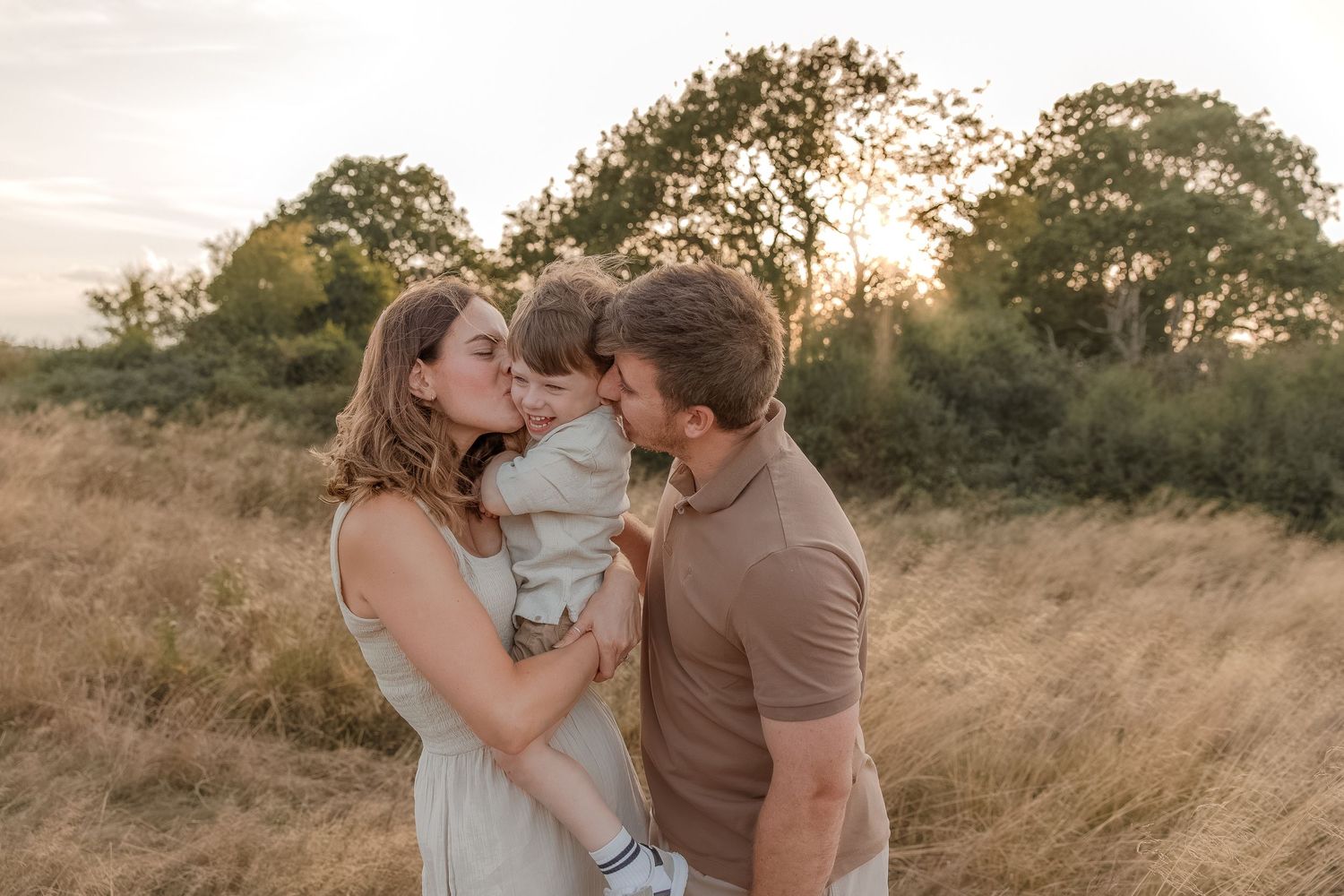 A Cotswolds Family Photographer captures a young family with parents kissing their toddler's cheeks in Snowhill, Cotswolds.