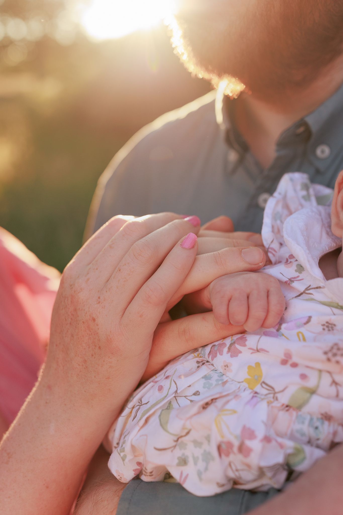 Close-up of parents gently holding their newborn baby's tiny hand in warm golden sunlight in Oxford.
