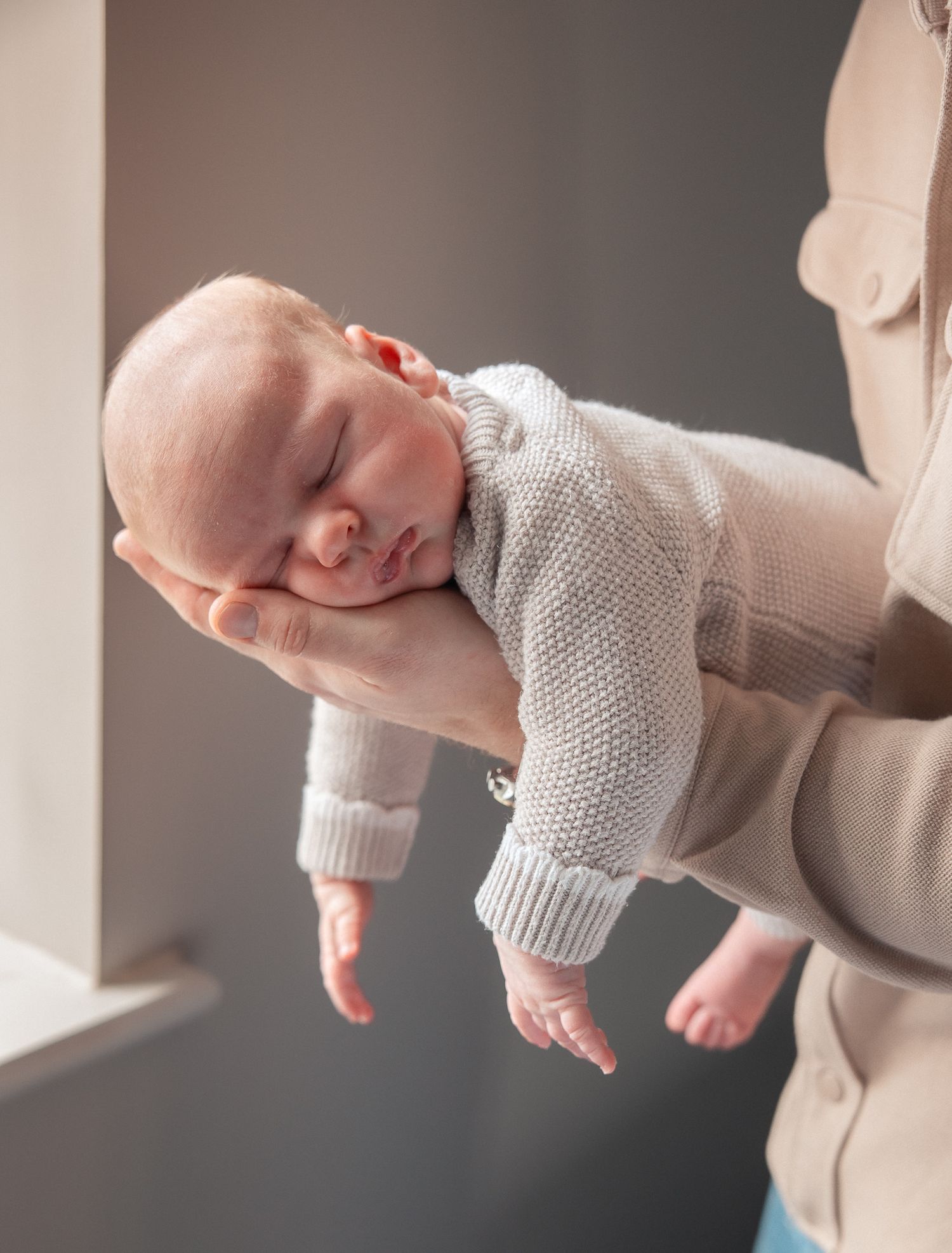 A newborn baby sleeping peacefully in the arms of dad, wrapped in a cosy knit in Henley-on-Thames.