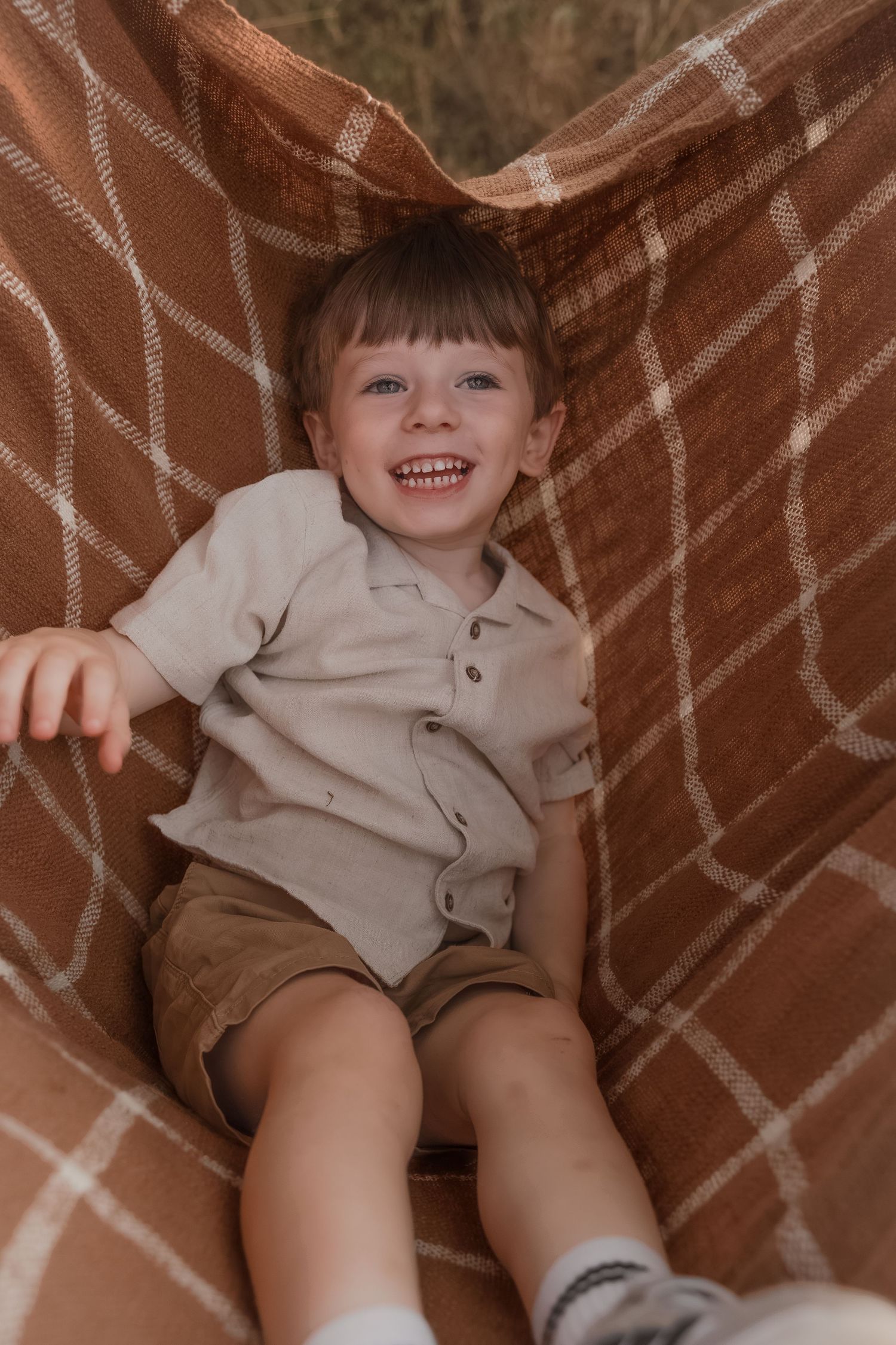 Family Photoshoot of a smiling young boy sitting in a brown plaid blanket in Bath, Somerset.