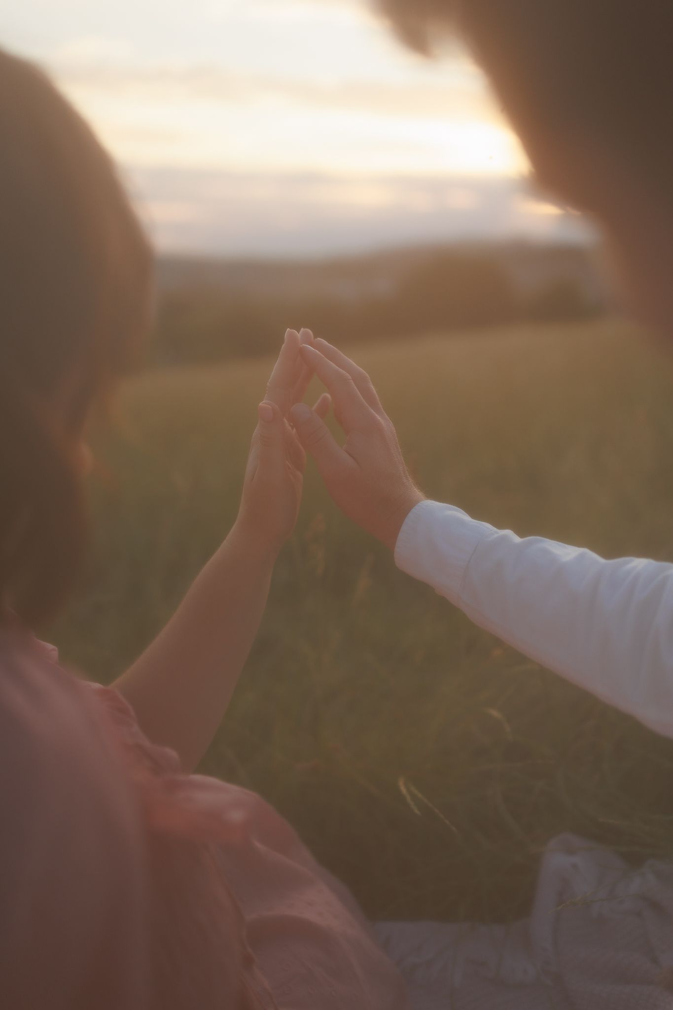 Two people touching hands at golden hour in a sunlit field during Maternity Photoshoot in Tooting, London.