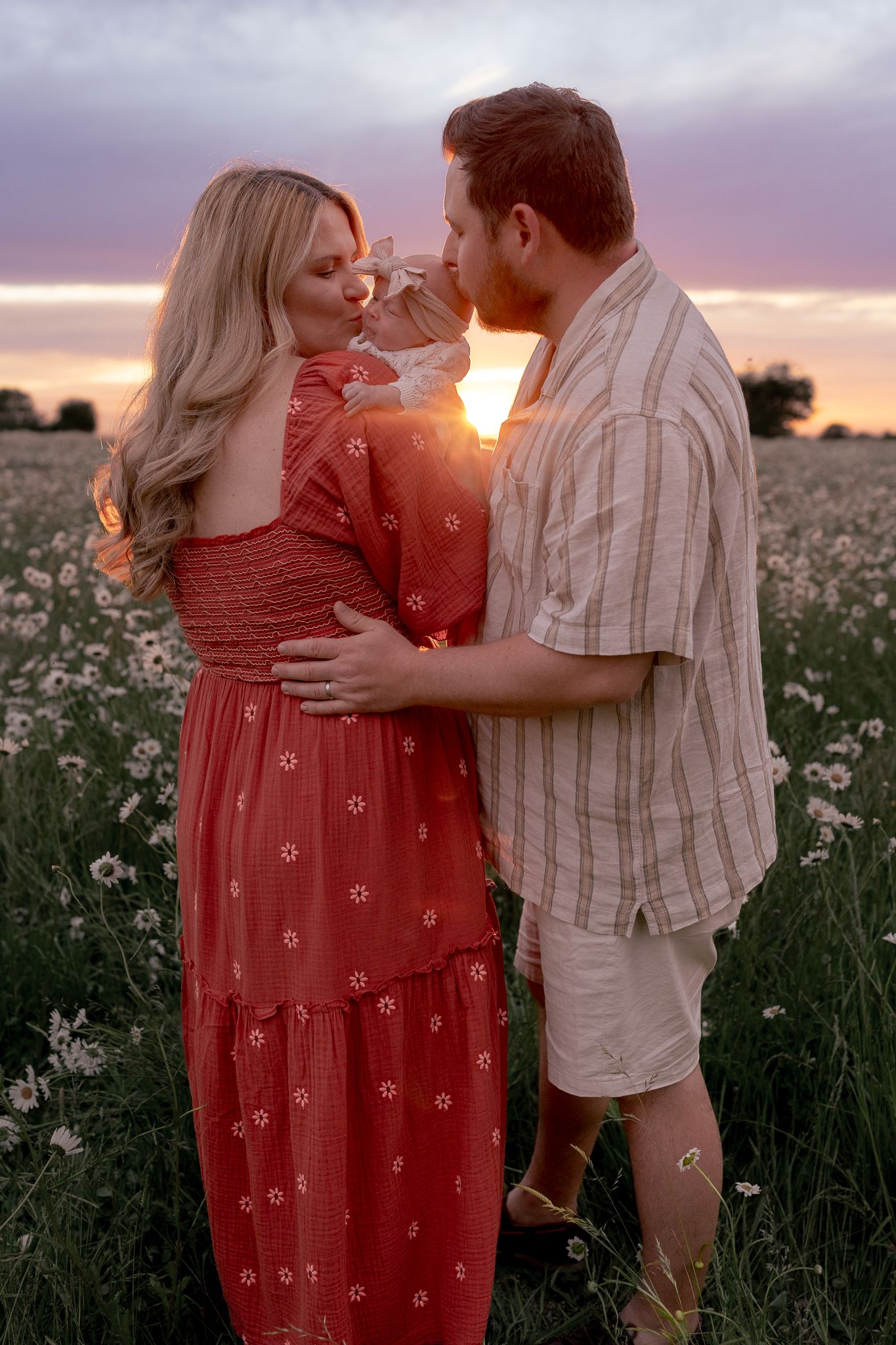 Couple embracing romantically in a wildflower field at golden sunset, woman in red floral dress.