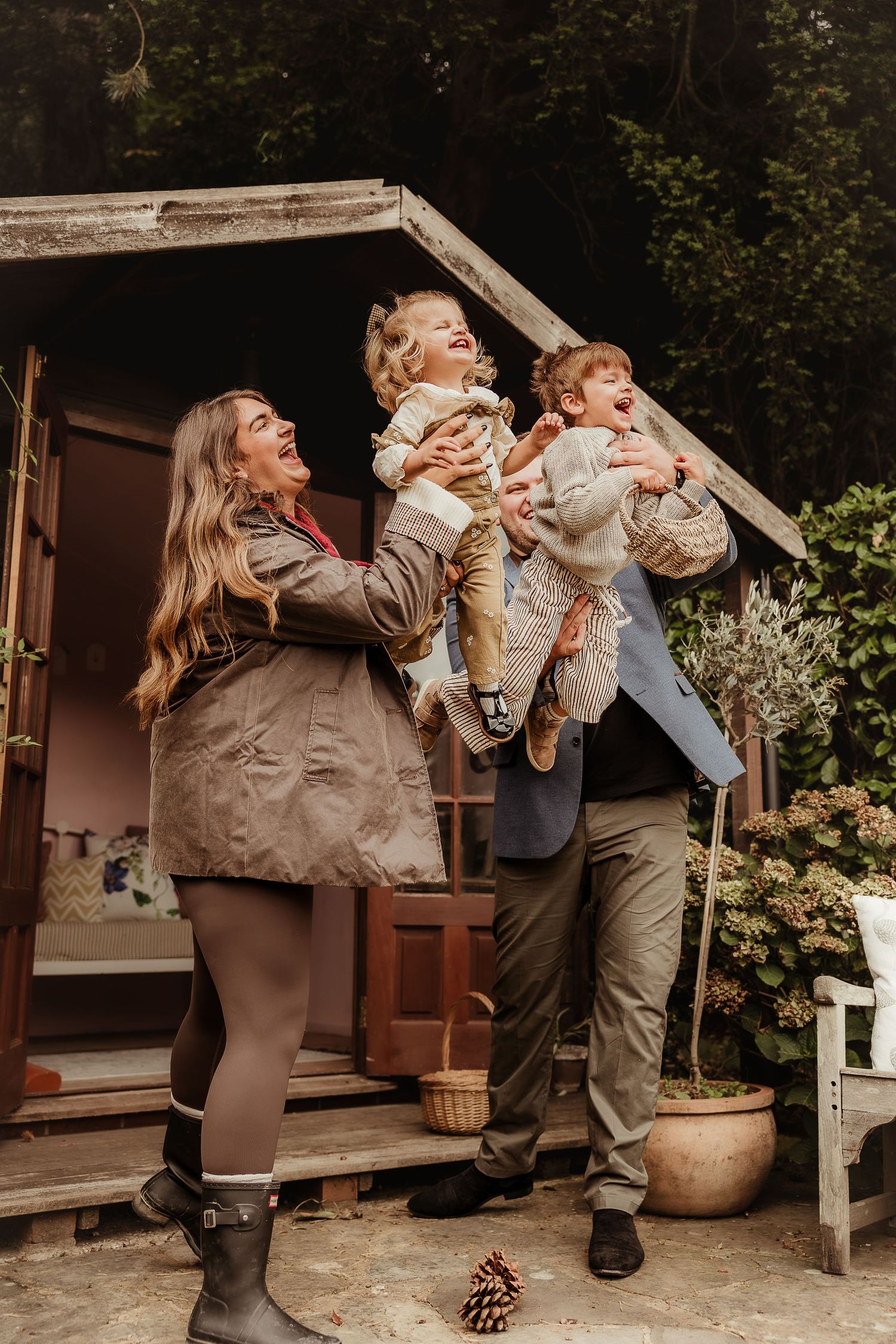 Family photoshoot of family with two young children laughing outdoors surrounded by lush greenery in Great Somerford.
