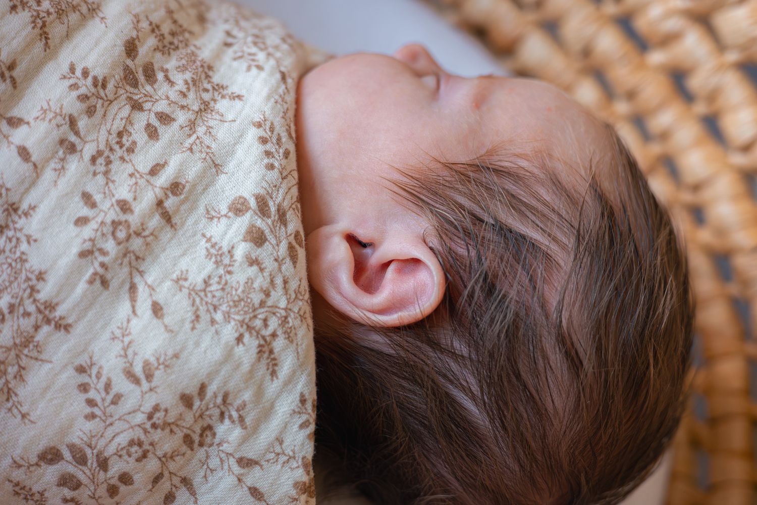 A close-up photo showing a babies tiny ear and thick black newborn hair. Stow-on-the-Wold, Cotswolds.
