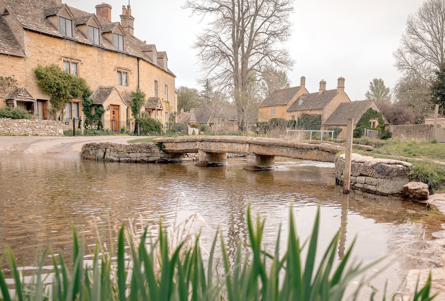 Charming Cotswolds village with stone bridge over calm river, historic cottages in Lower Slaughter, Cotswolds, UK.