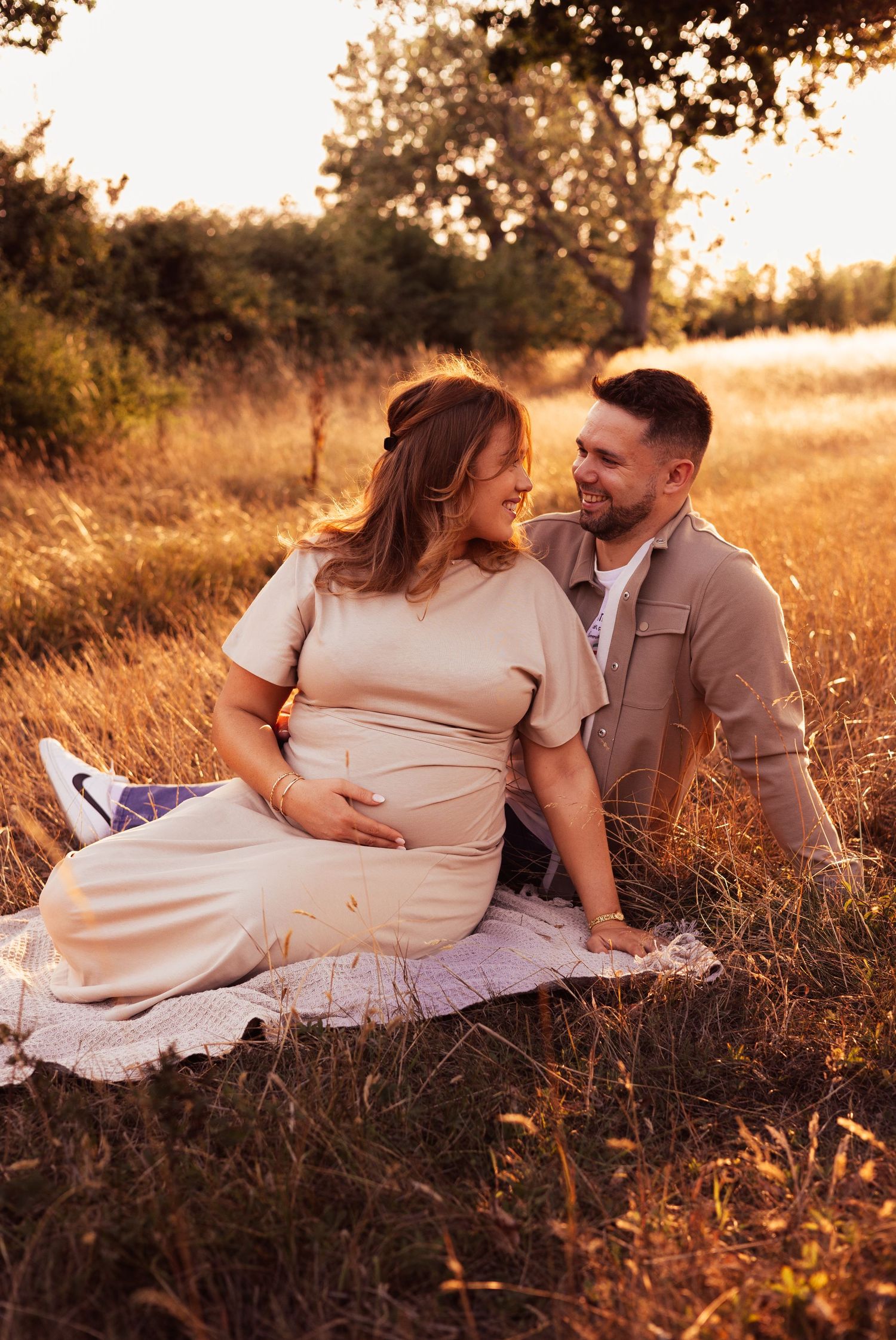 Couple relaxes in golden field during sunset maternity photoshoot in Beaulieu.