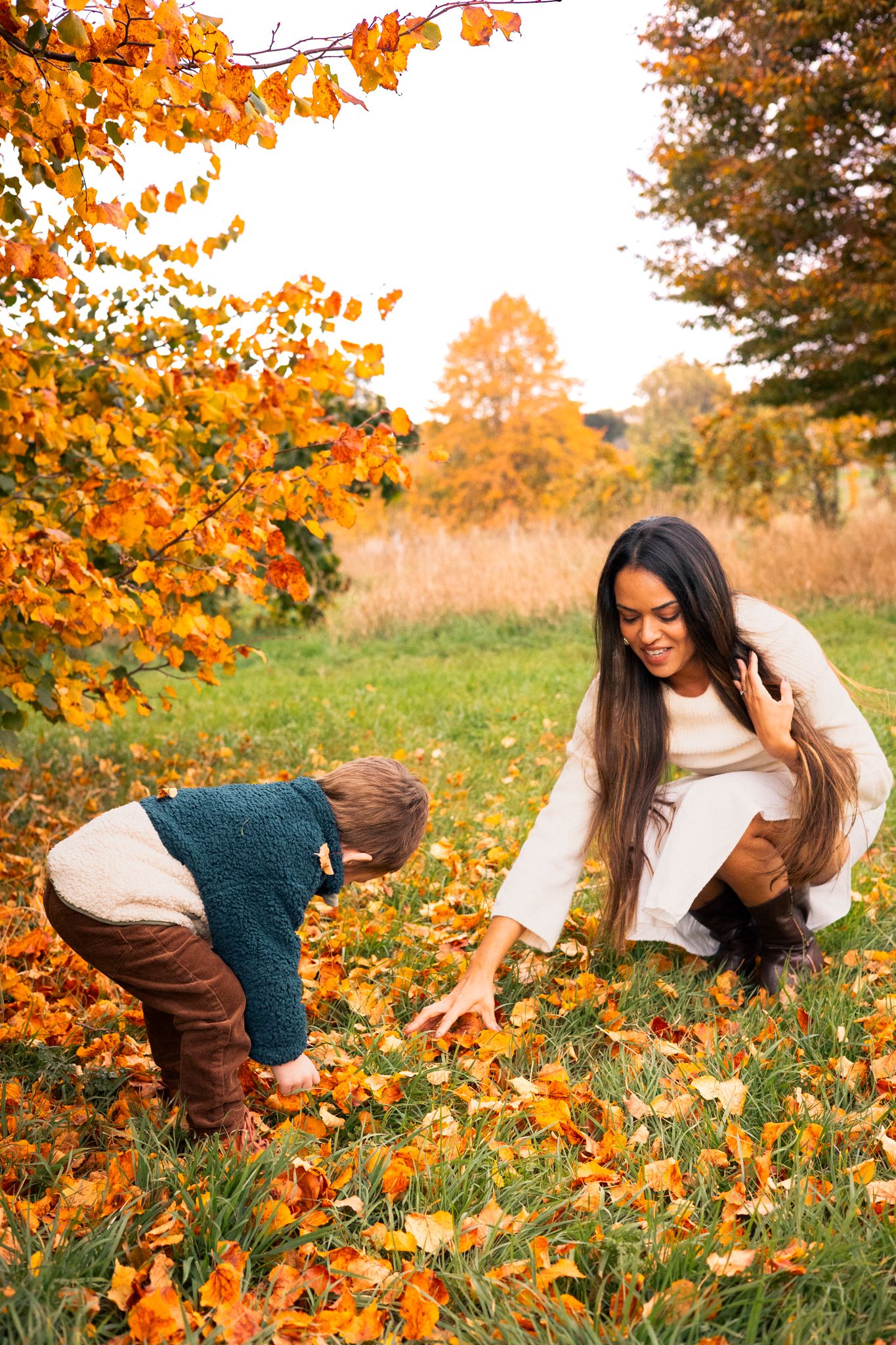 A woman and child playing with fallen autumn leaves during Autumn Mini Session in a park surrounded in Swindon, Wiltshire.
