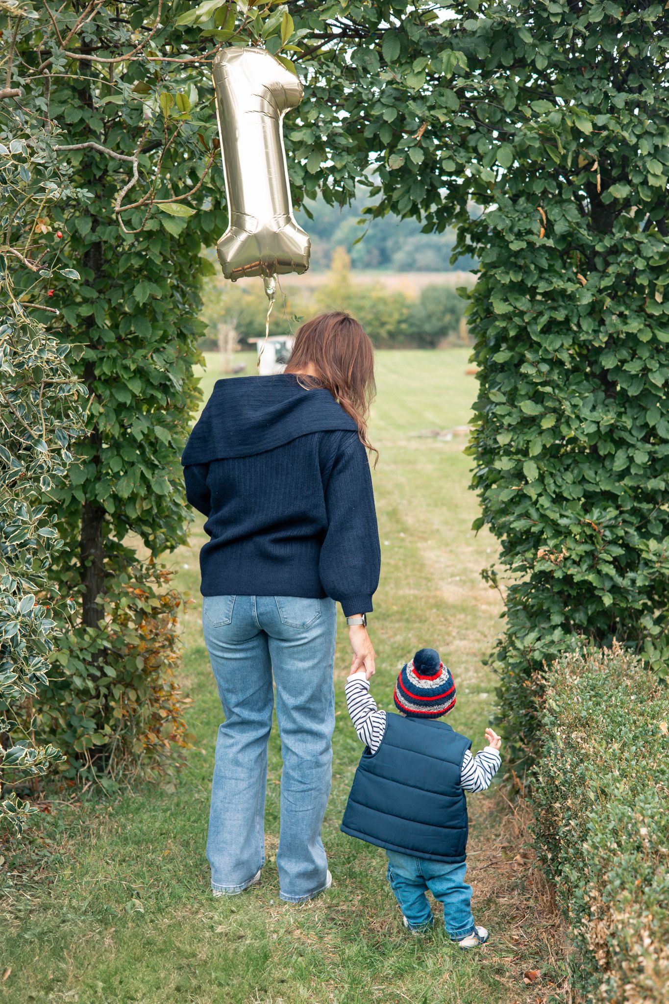 Parent and child explore together among rows of green hop vines in a field in Barton-on-Sea.