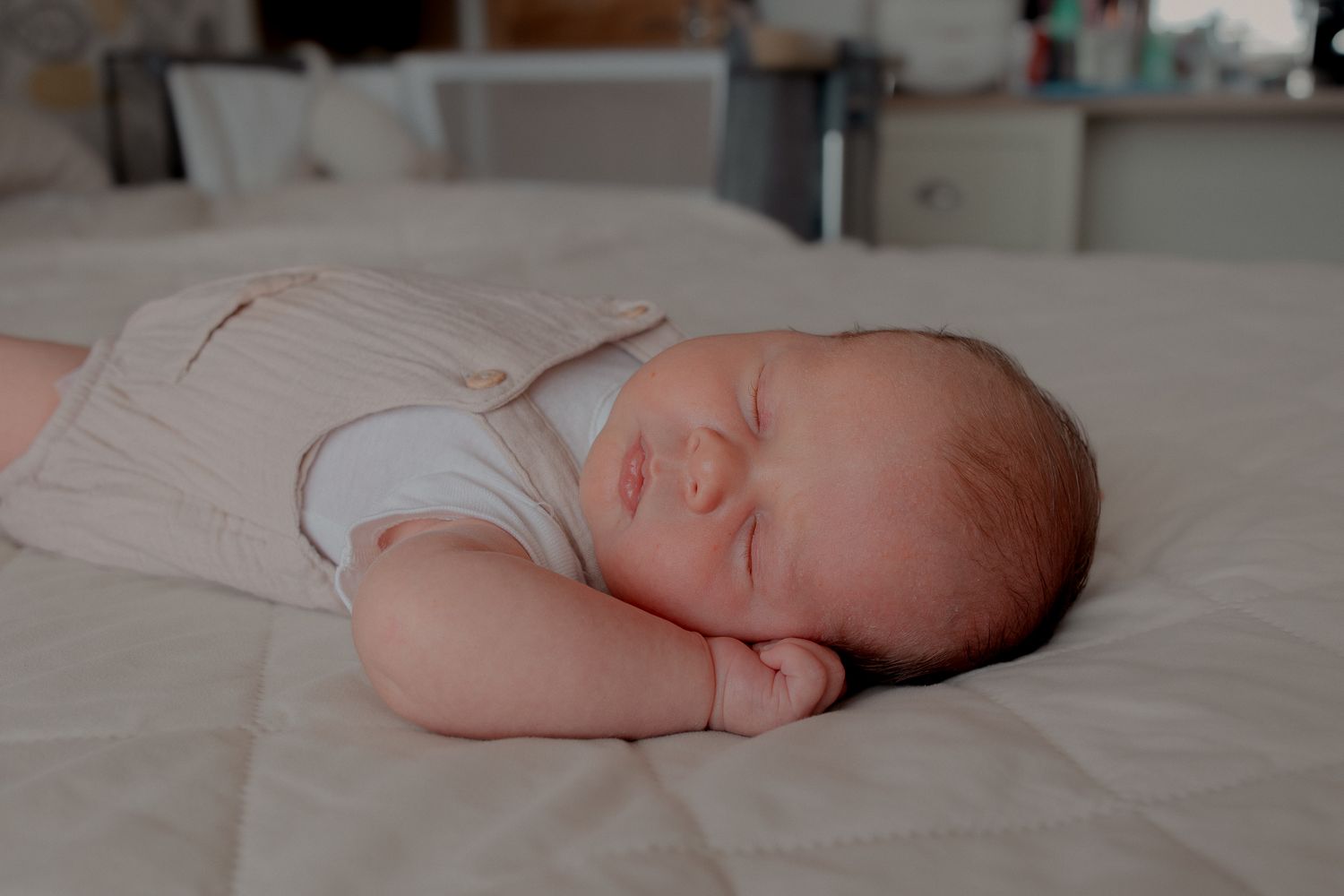 Newborn baby sleeping peacefully on a white bed, lying on their side with tiny hands tucked under their cheek in Clevedon, North Somerset.