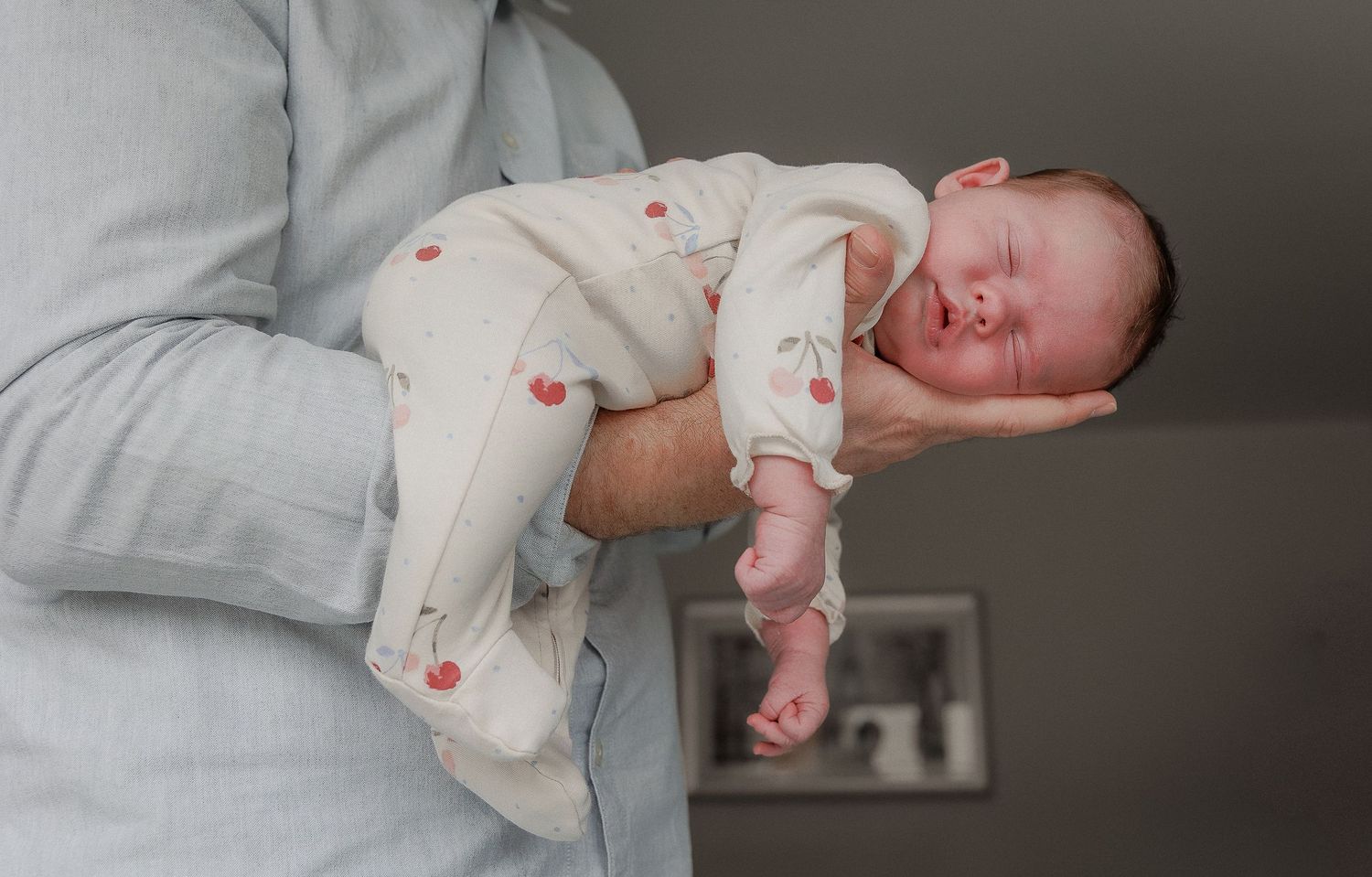 Newborn Photographer takes photo of father holding sleeping newborn baby in Cirencester Cotswolds.