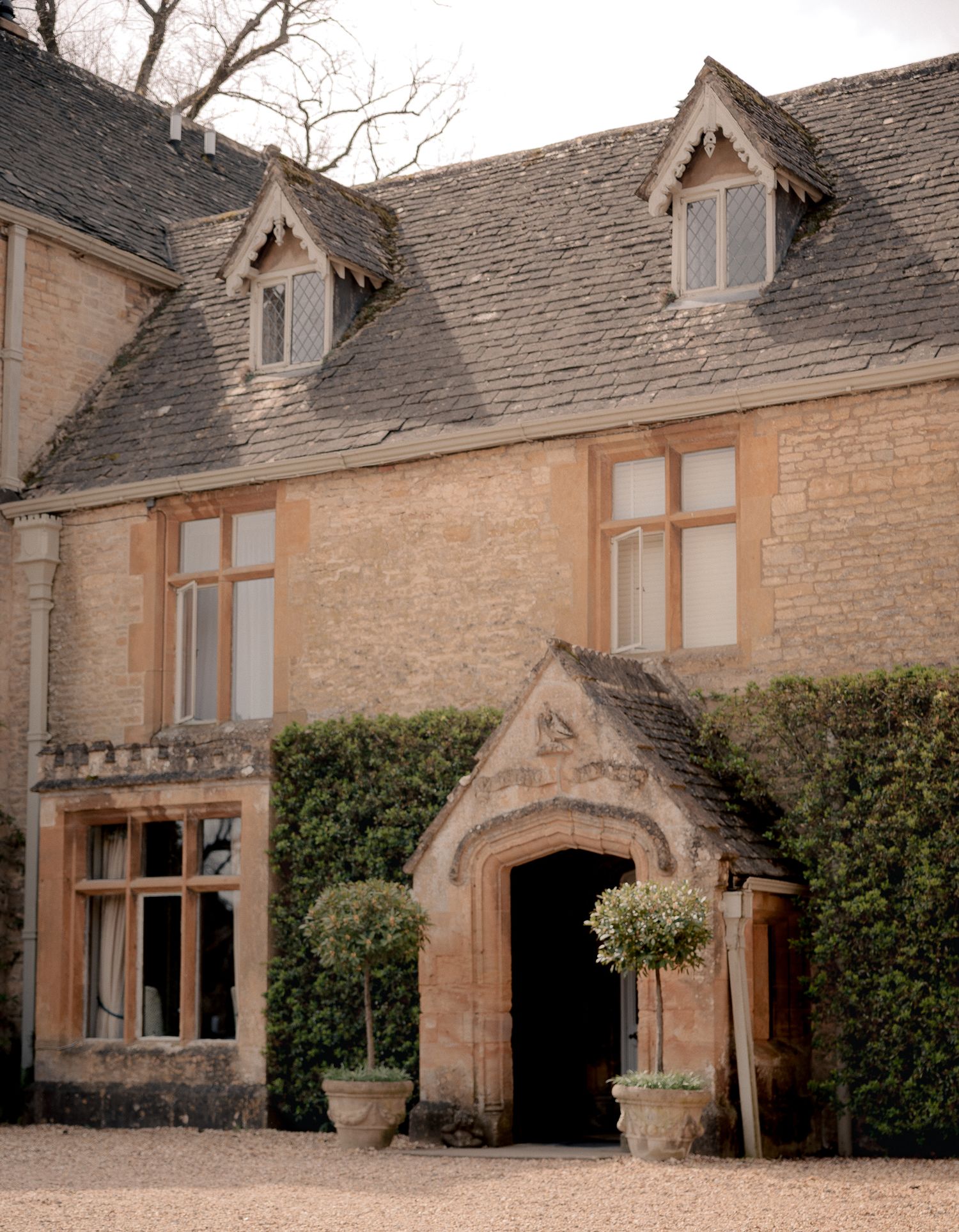 Lords of the Manor Hotel with arched entrance, dormer windows, and manicured topiary trees in terracotta pots in Upper Slaughter.