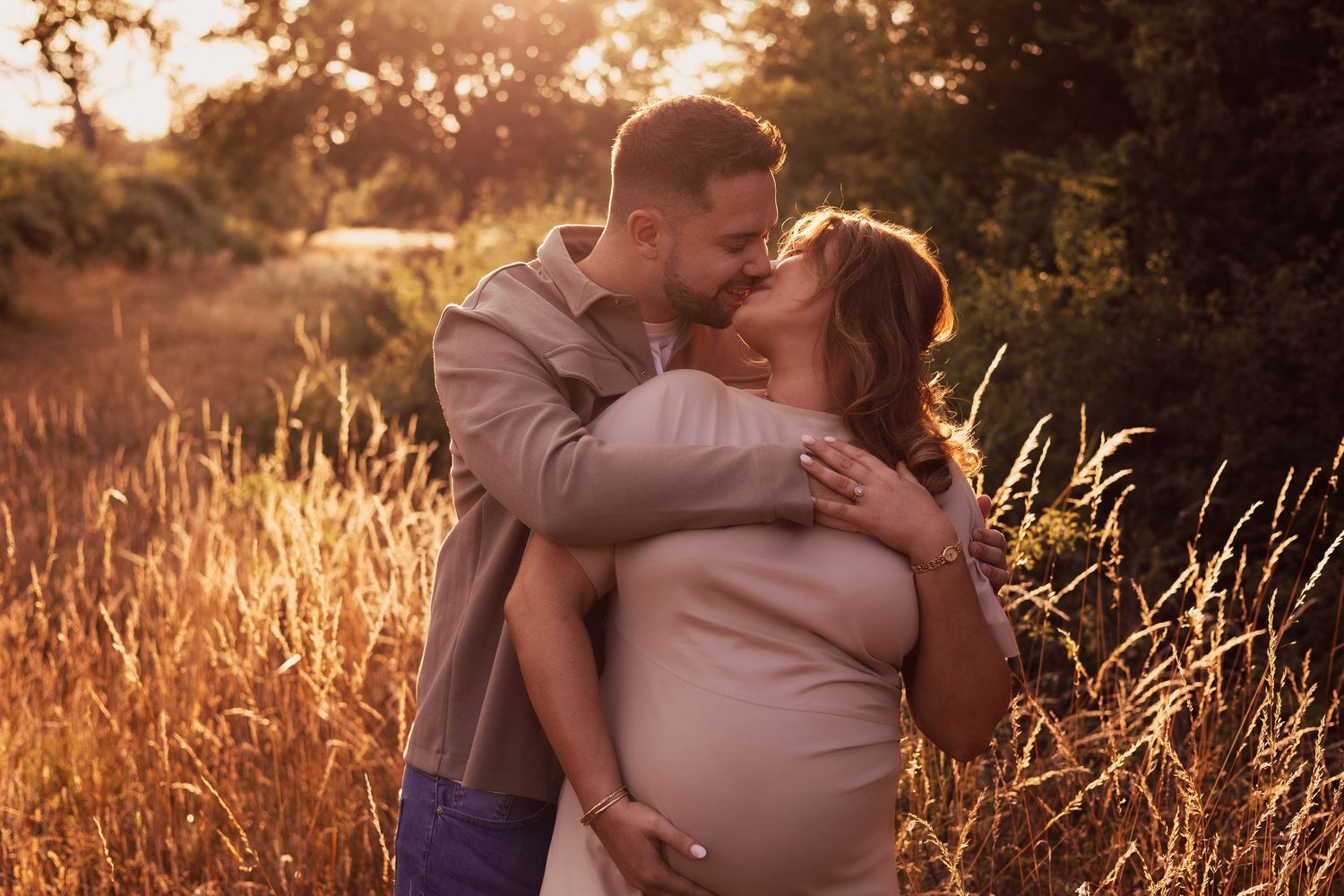 Intimate maternity photos captured in warm sunset light among tall grass.