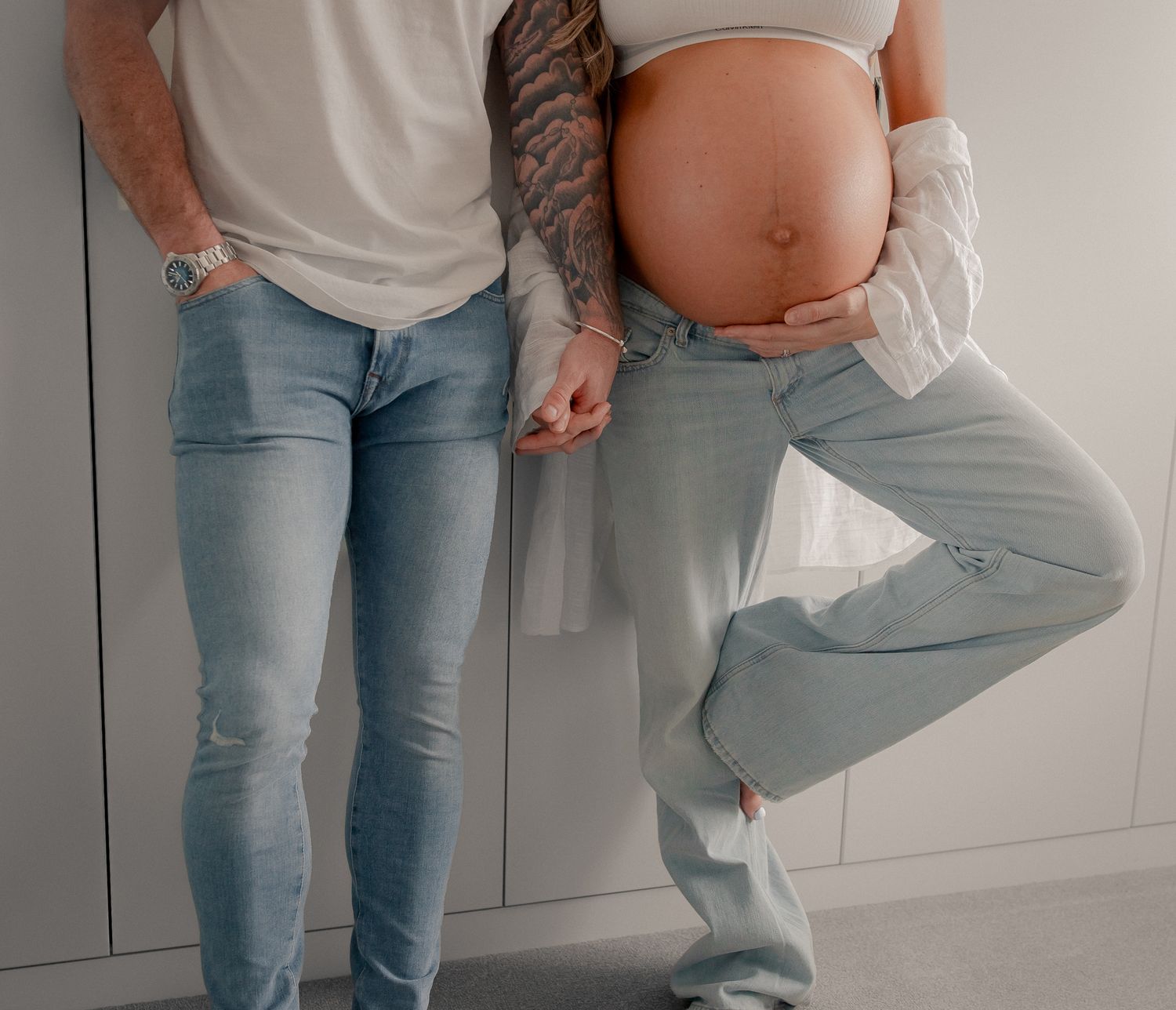 Couple posing for maternity photo, pregnant woman showing baby bump, both wearing light blue jeans in Faringdon.