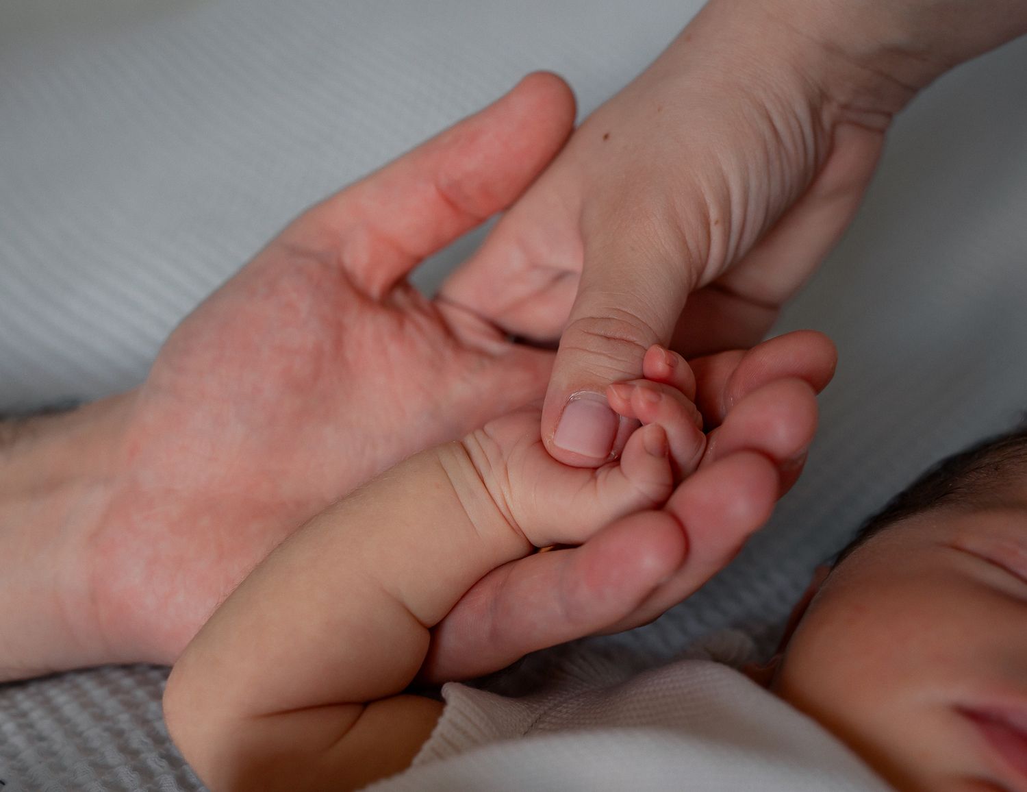 Newborn baby grasping adult finger in open palm, close-up of tiny infant hand holding parent's finger in Cirencester, Cotswolds.
