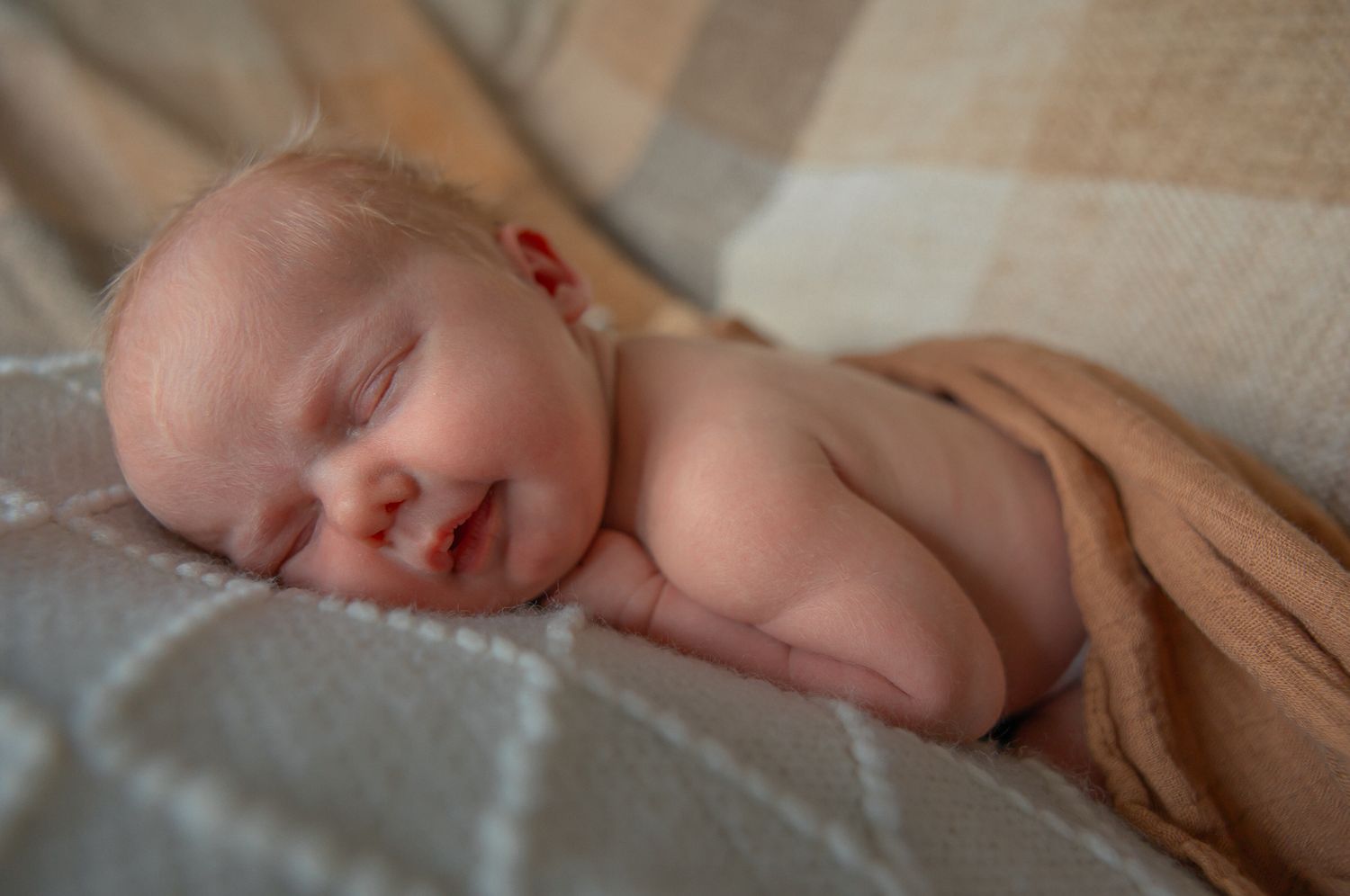 A sleeping newborn baby rests peacefully on soft beige bedding. Northleach, Cotswolds