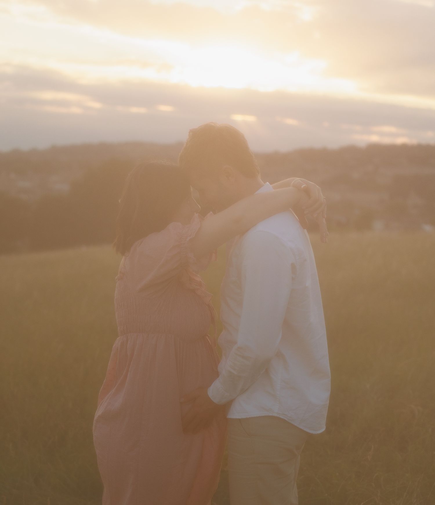 Couple embracing at sunset in a green meadow with golden light during Maternity Photoshoot in Eton.