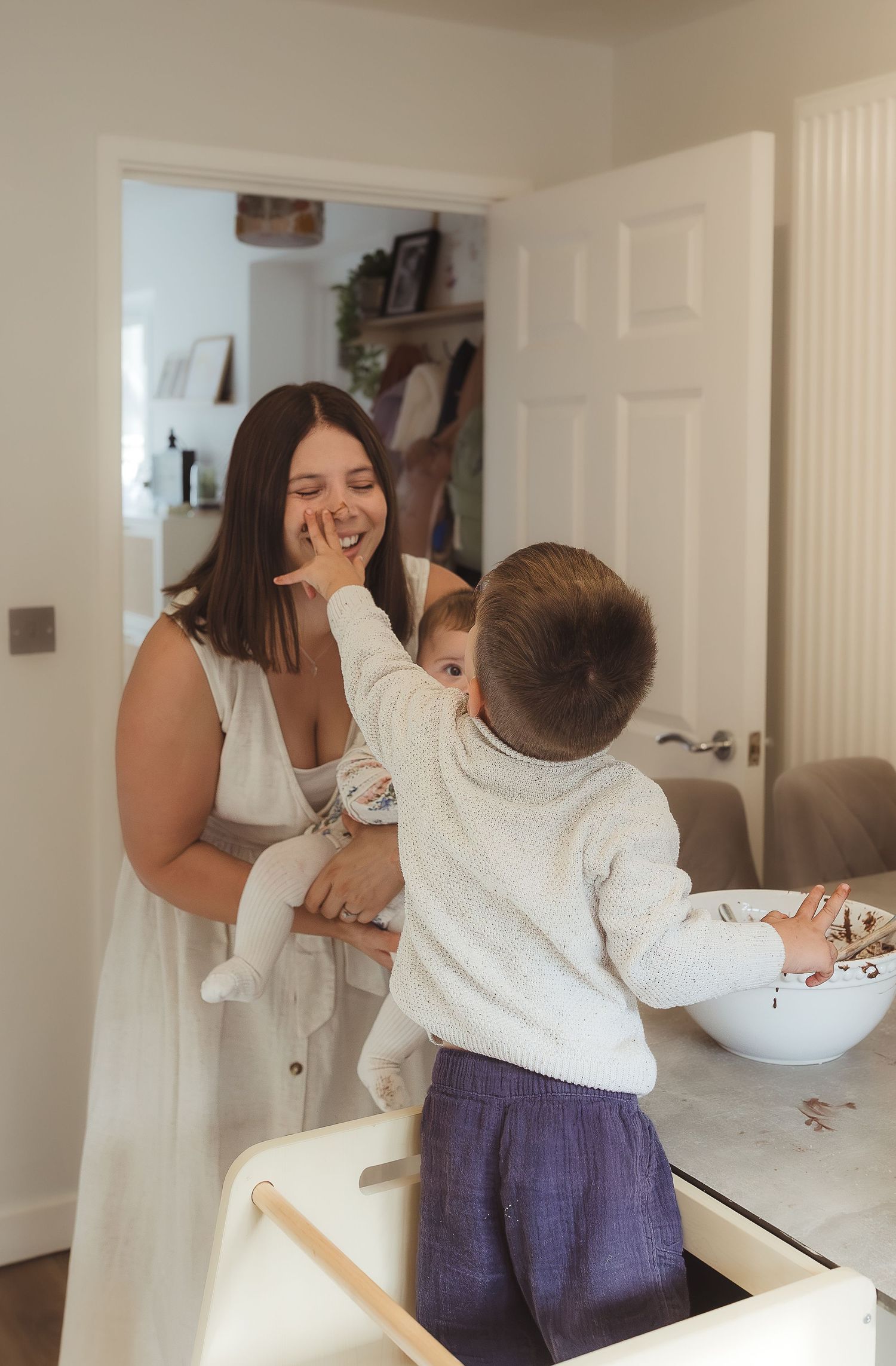 Storytelling photoshoot of a smiling mother while a toddler reaches up to touch her face with cake mix in Broadway, Cotswolds.