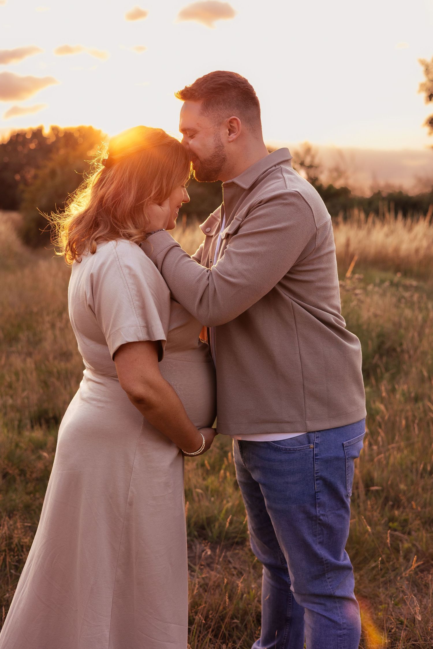 A couple embraces tenderly in a golden sunset field cradling first baby maternity bump in Milford-on-Sea.