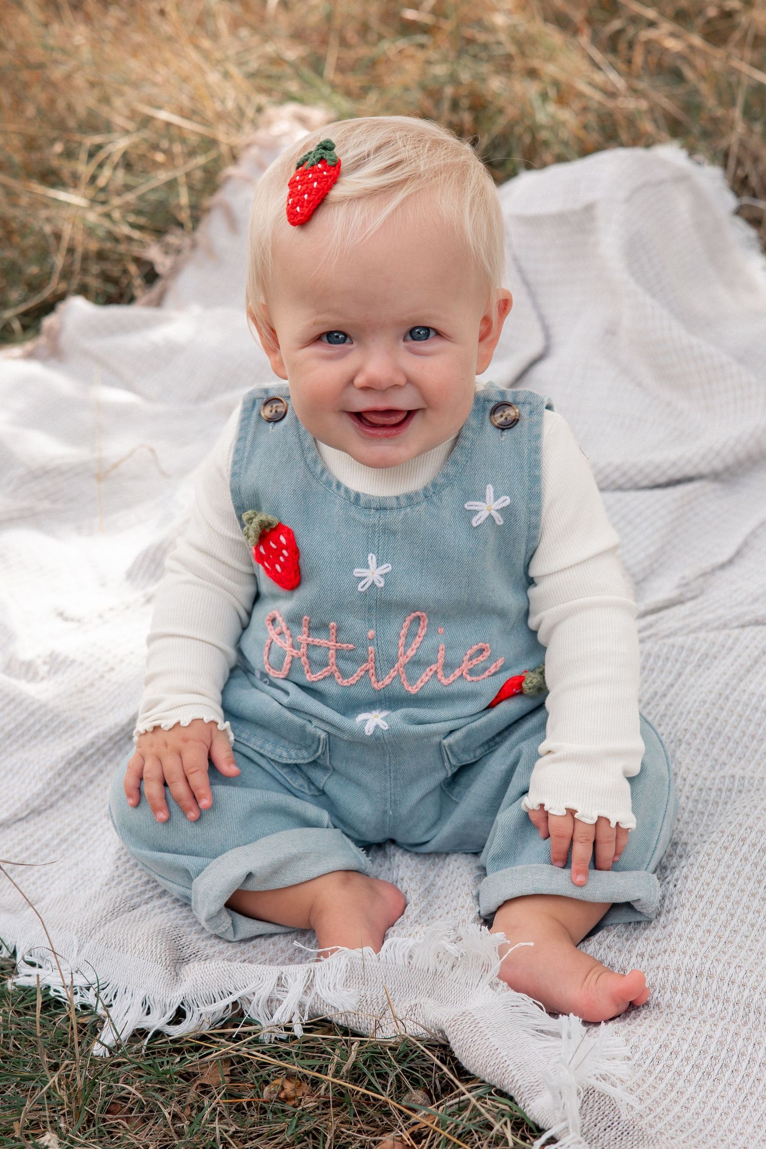 Baby wearing blue outfit with strawberry accessories lying on white blanket. Slaughter, Cotswolds